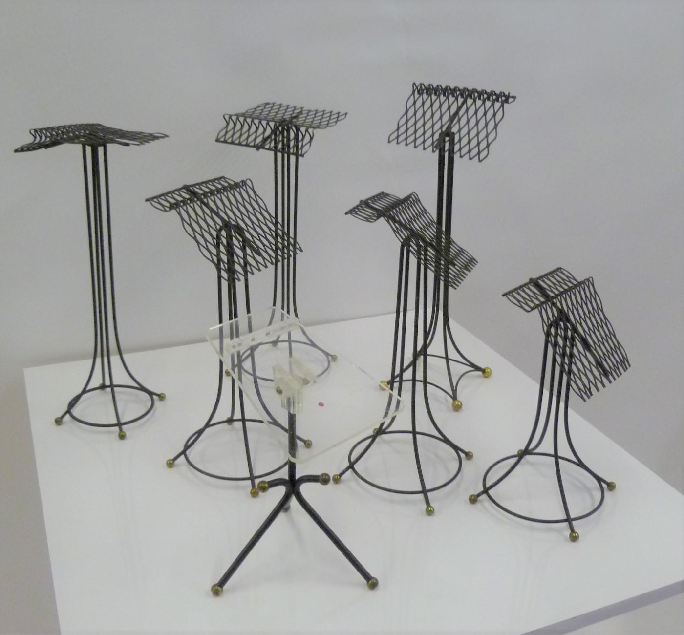 From the 1930s-40s sculptural group of 7 black metal store display stands, most likely for ladies shoes. Three different styles: one with a Lucite top, one with Eiffel tower base and 5 different heights with rounded base. In very good original