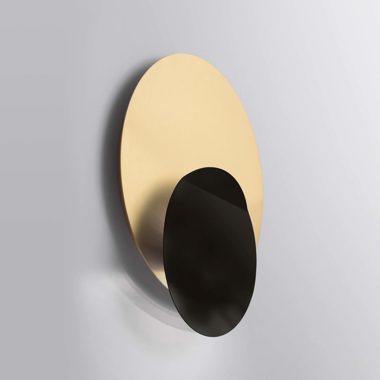 A fascinating interplay of shadows and light distinguishes this exquisite sconce of strong sculptural allure. The two disks in metal have different finishes that reflects the light from the hidden bulb and change hues in different times of the day