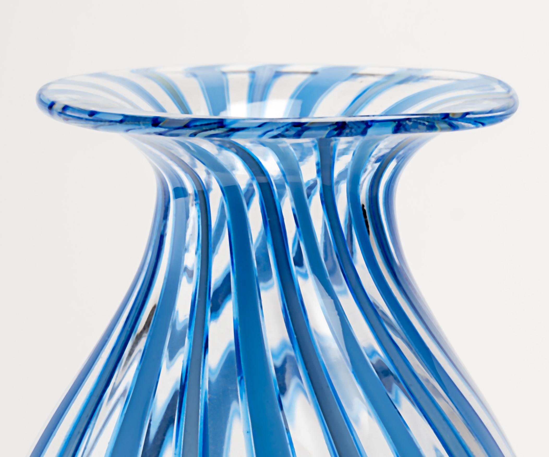 Jeremiah Jacobs, a skilled glassblower, has crafted a stunning blown glass piece using the filigrana cane technique. The artwork features a mesmerizing combination of blue and clear stripes, showcasing the artist's expertise in manipulating