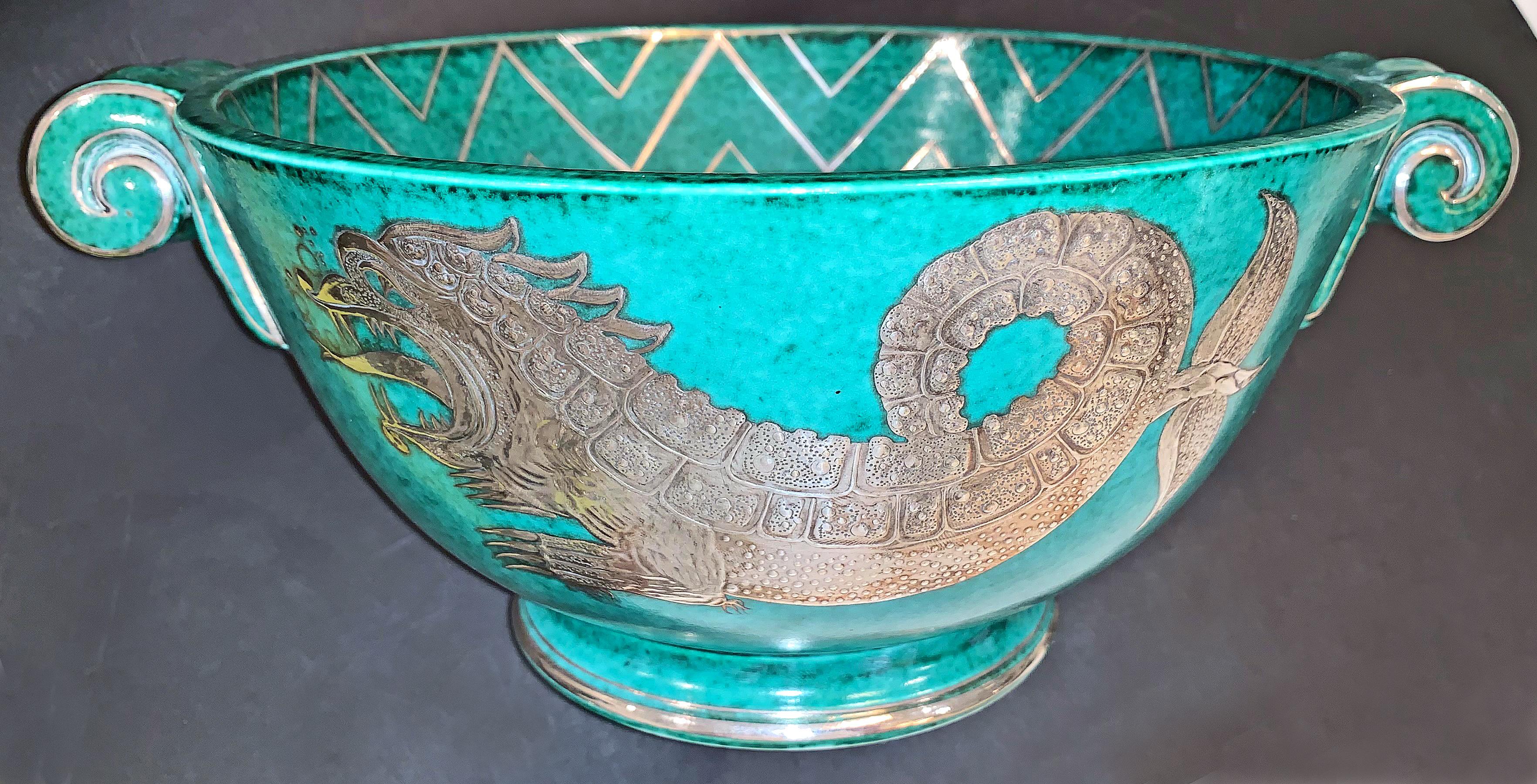 Stunning and gorgeous, and the only example we have seen, this Art Deco porcelain bowl -- glazed in a blue-green hue and finished with carved, silver overlay -- depicts a fantastic sea dragon on the exterior, and is finished with an elaborate,