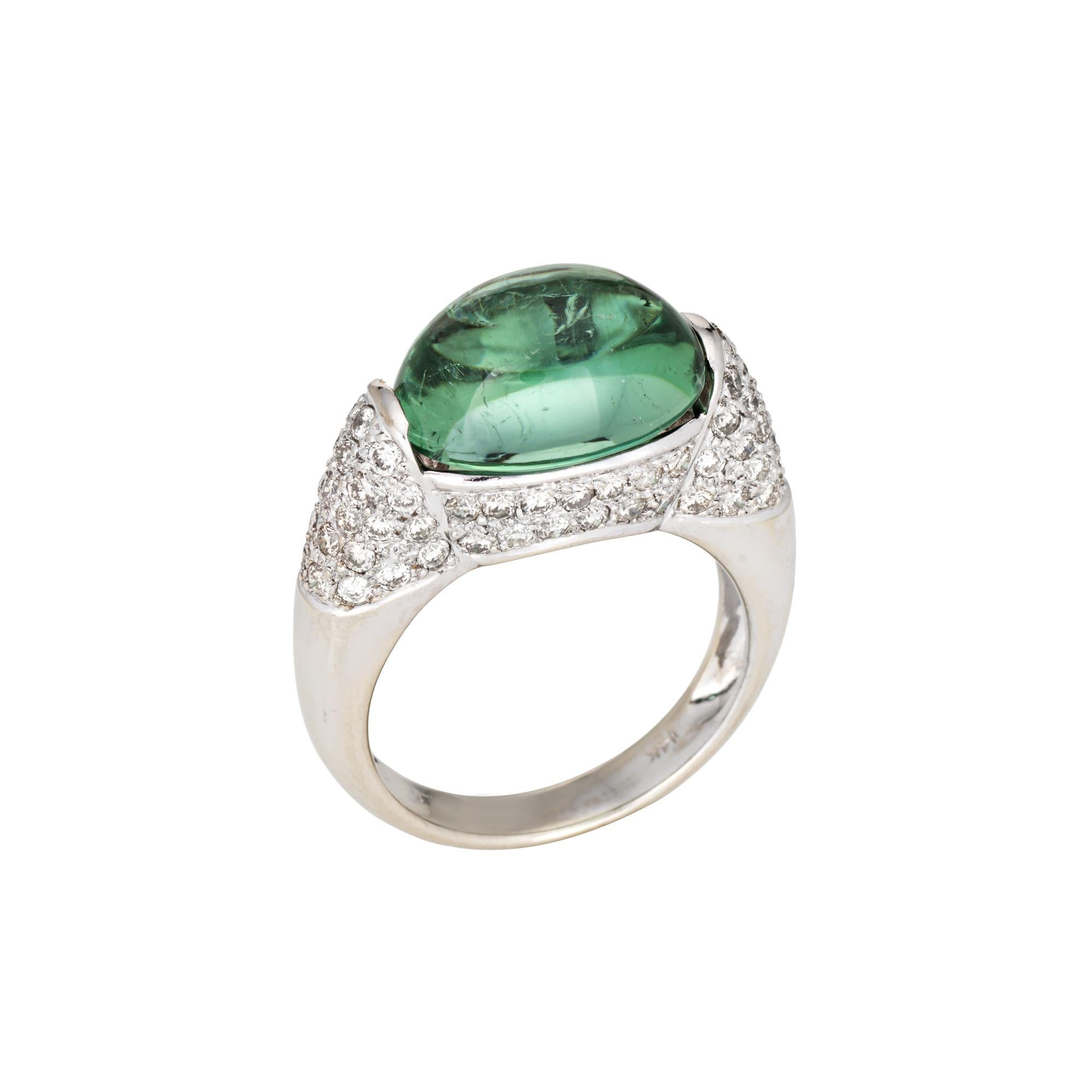 Elegante anillo contemporáneo de turmalina verde y diamantes elaborado en oro blanco de 14k (hacia la década de 2000).

La turmalina verde de talla cabujón engastada en el centro mide 12 mm x 9,5 mm, acentuada con unos 0,50 quilates de diamantes (de