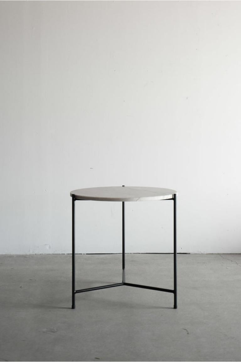 La table d'appoint Sea Pearl met en valeur la beauté organique du quartzite naturel. Le plateau en quartzite présente des veines ondulées dans des tons clairs et neutres, créant un effet serein et apaisant. La base en acier noir mat, offre un accent