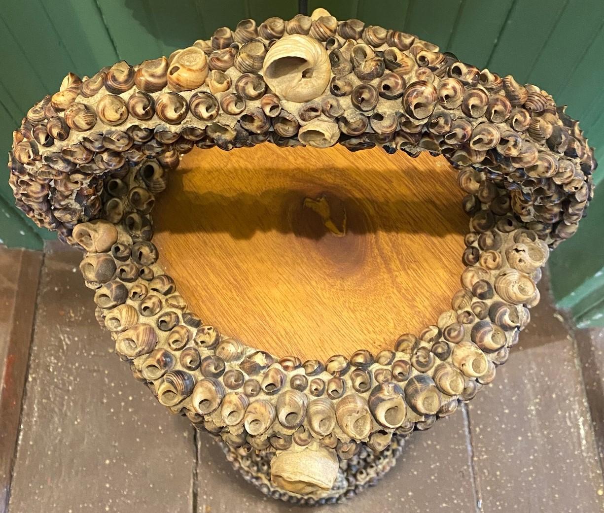 Antique Edwardian Folk Art Sea Shell Decorated Wooden Stand, circa 1920, having a variety of North American periwinkles, moon snails, oysters, etc. mounted on a hand-crafted pedestal stand with arched handle: originally a stand for an ash tray but