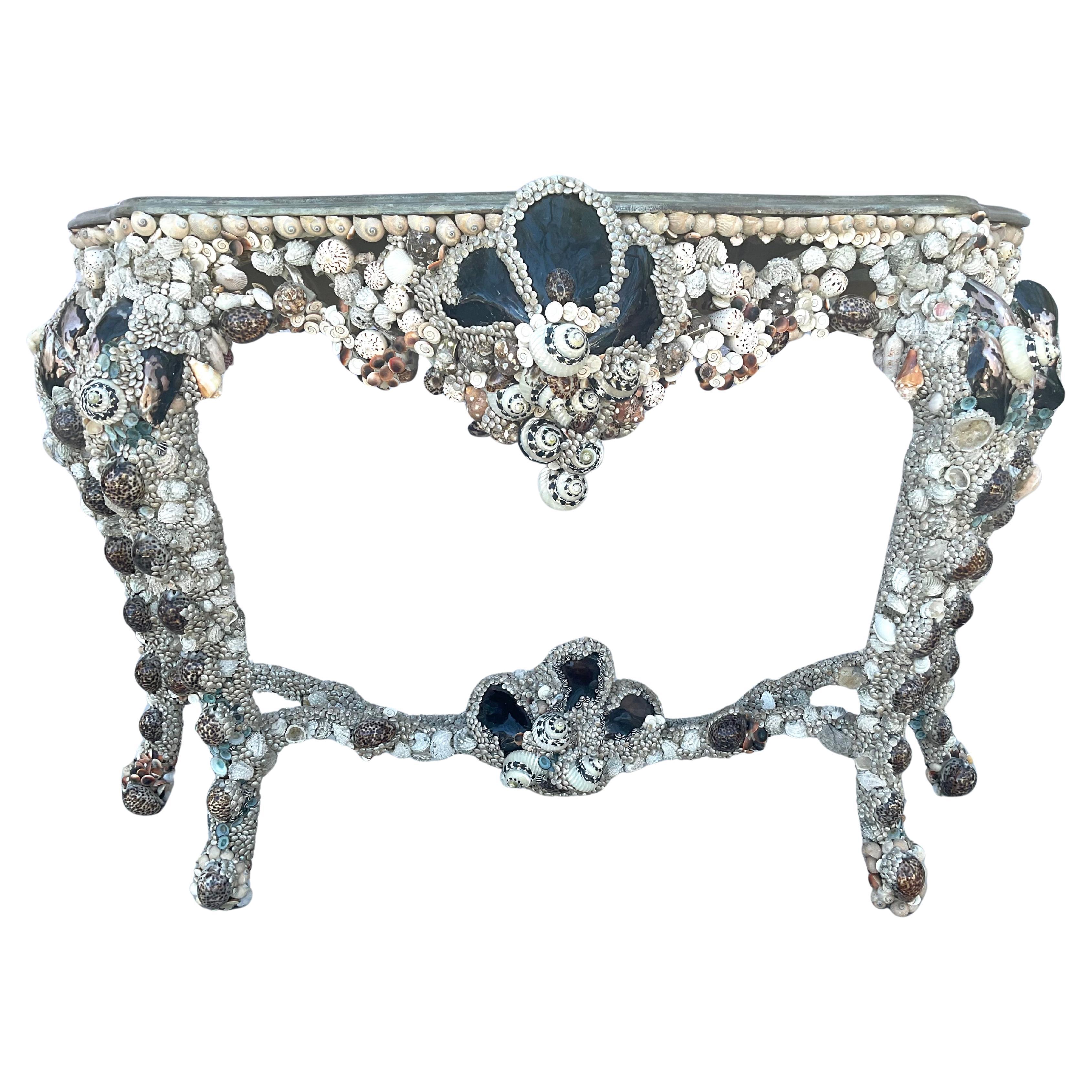 Vintage Grotto Style Seashell Encrusted Console Table is a striking and unique piece that combines a perfect balance of clean lines and organic forms. The base of the table is made of wood and features a serpentine front  with cabriole legs. The