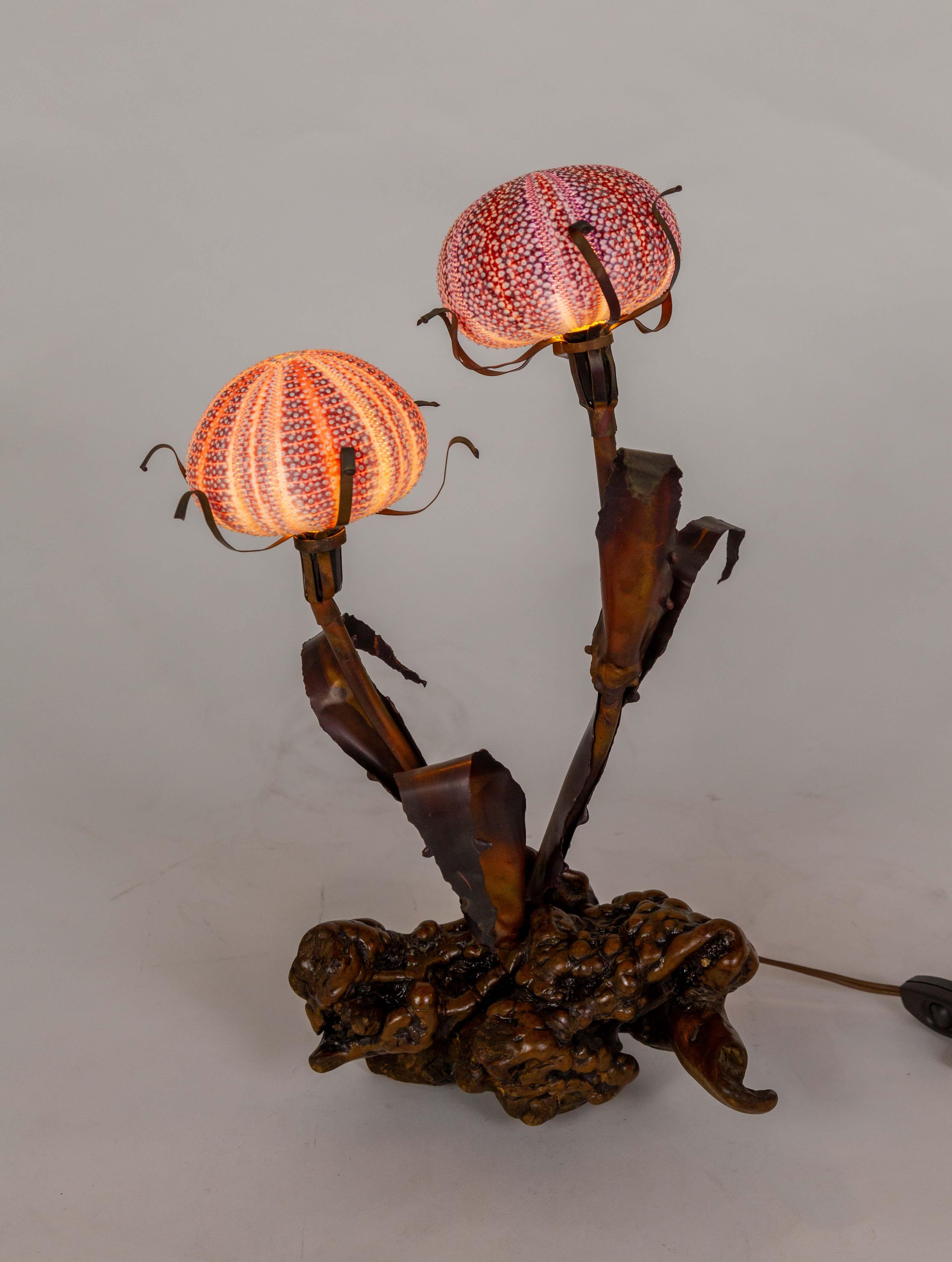 A sculptural table lamp with a burl wood base, copper leaves, and stems holding two sea urchin shells. A beautifully organic design by Curtis Jere. The urchin shells act as shades for two lights that sit atop the stems with delicate copper S-curves