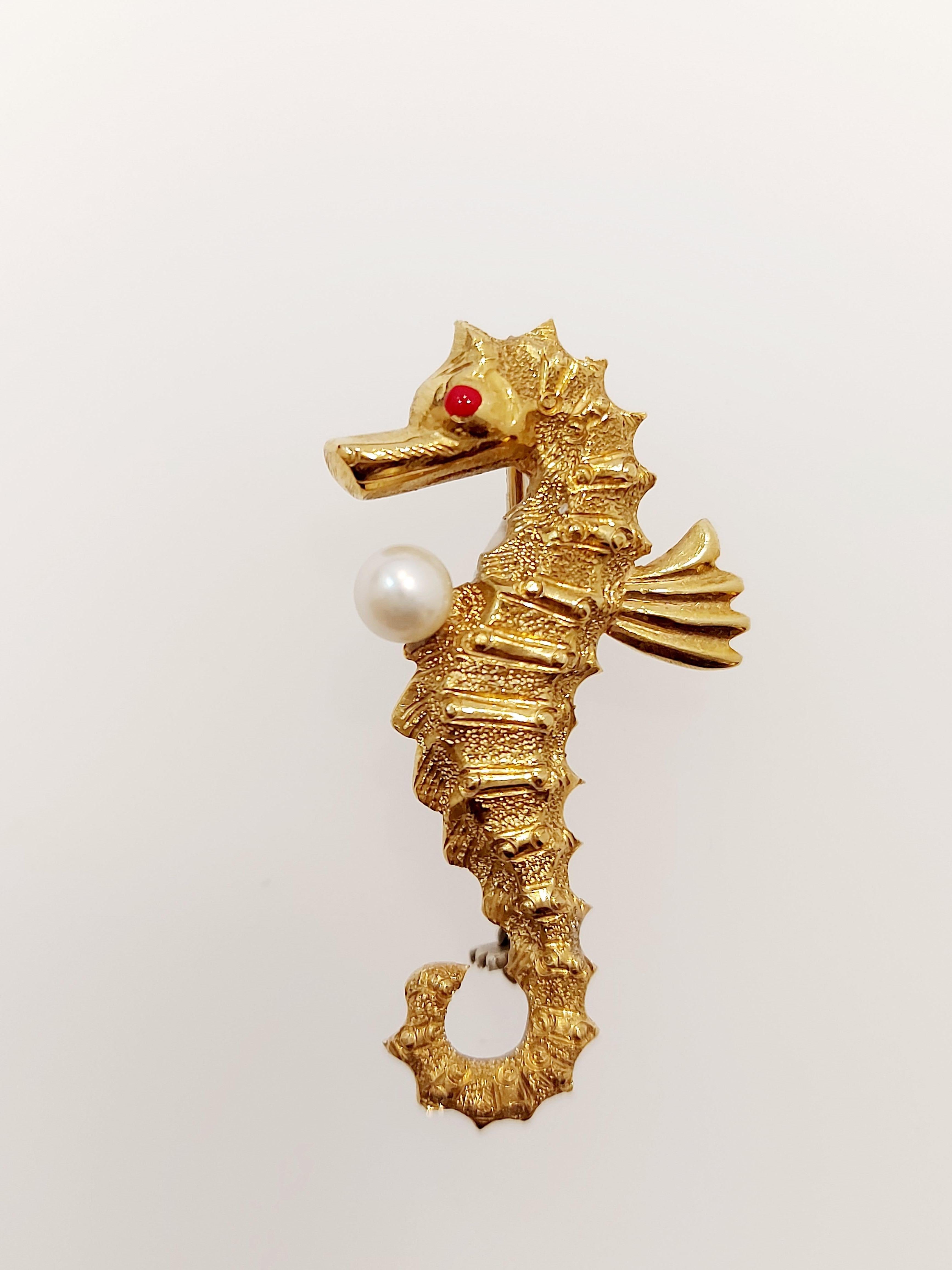 A seahorse brooch set pearl and with red eye, hallmarked 18ct gold textured body detail with a 4mm cultured pearl and red enamel eye.