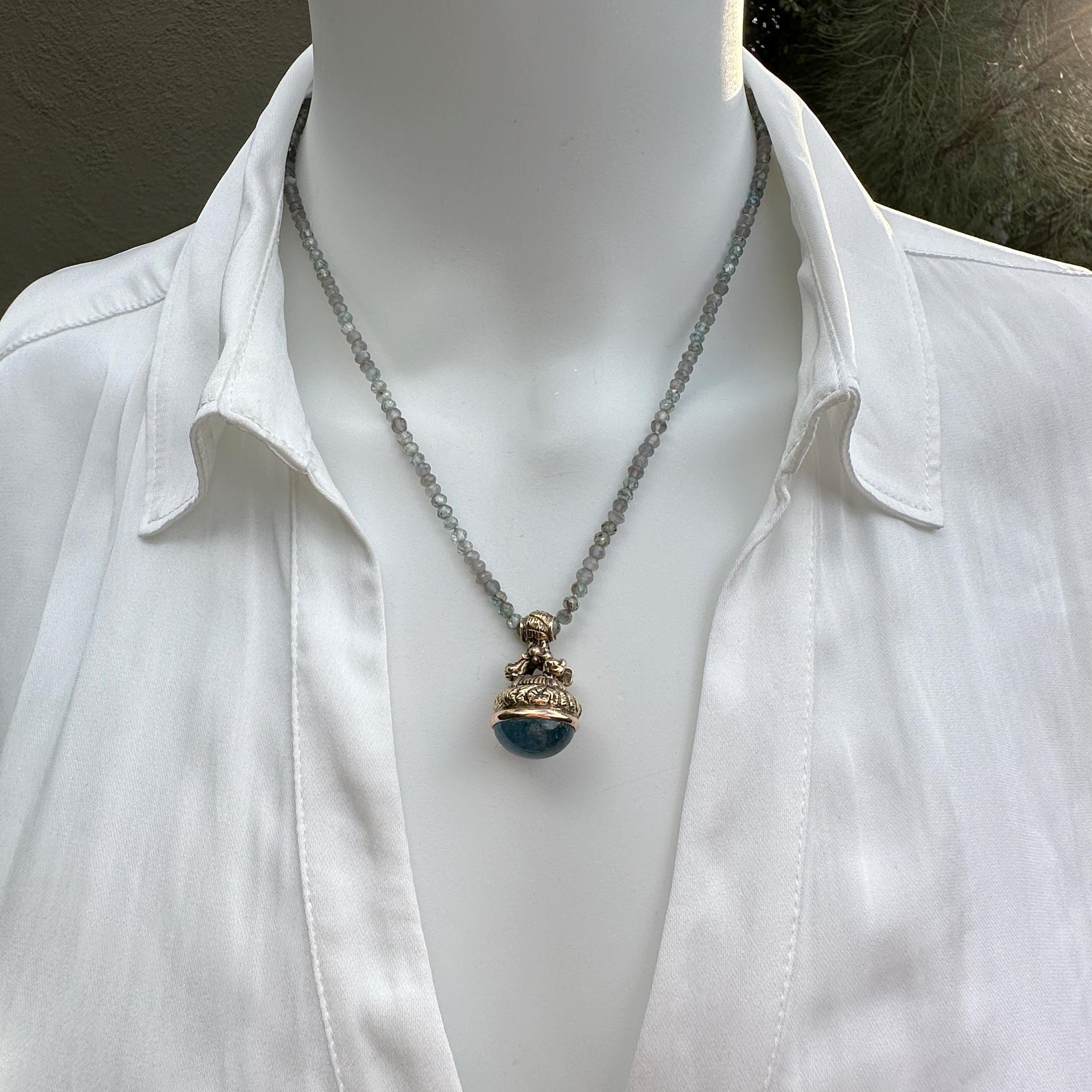 Eytan Brandes cast an old bronze seal in 14 karat yellow gold and converted it to a pendant, holding an oval cabochon of natural stormy blue aquamarine.  It hangs on a shimmery necklace of blue and grey beads -- a twilight mixture of moonstone and