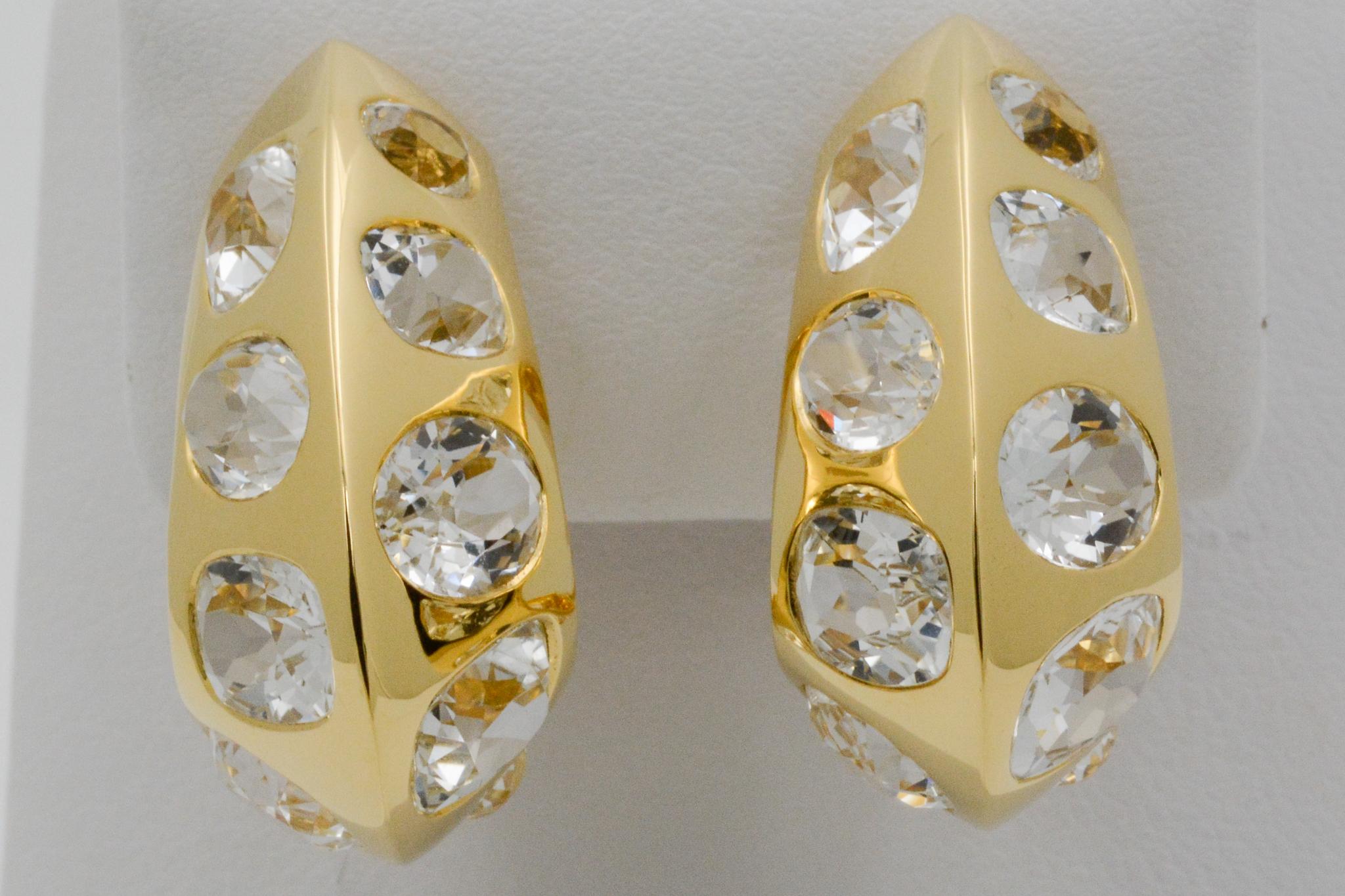 These Seaman Schepps 18k yellow gold Antibes earrings feature white topazes. The earrings have a J hoop style with a peaked dome shape and polished finish. The earrings also have clip backs and are signed Seaman Schepps.