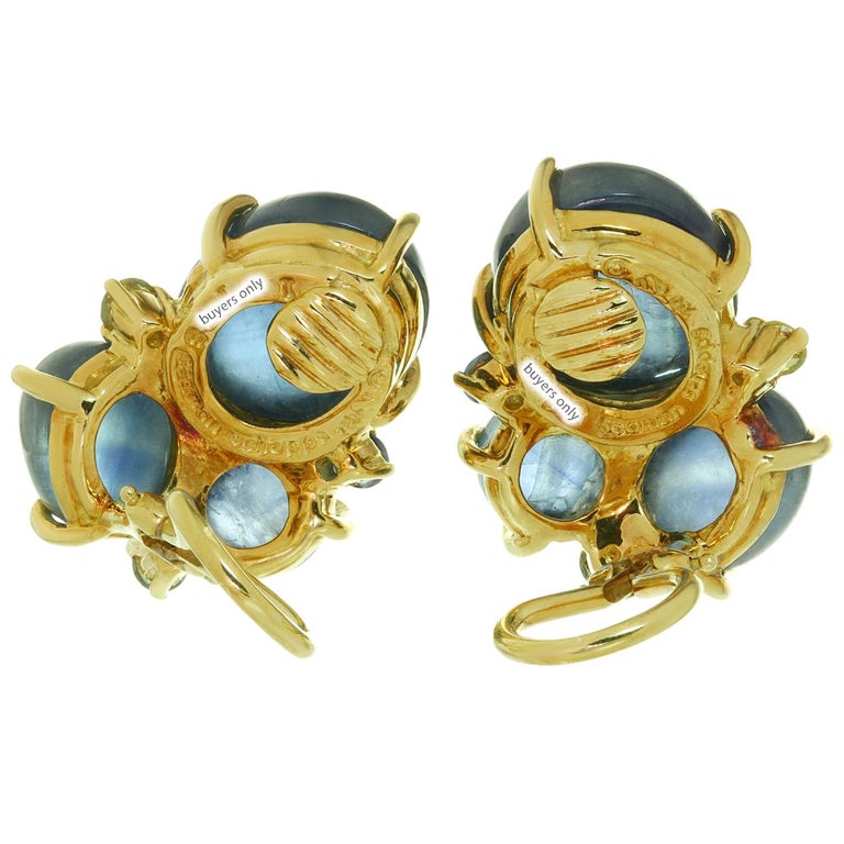 These fabulous Seaman Schepps clip-on earrings are crafted in 18k yellow gold and feature round and oval sapphires and peridots. The gemstones are genuine and feature typical inclusions. Made in United States circa 1980s. Signed and numbered.