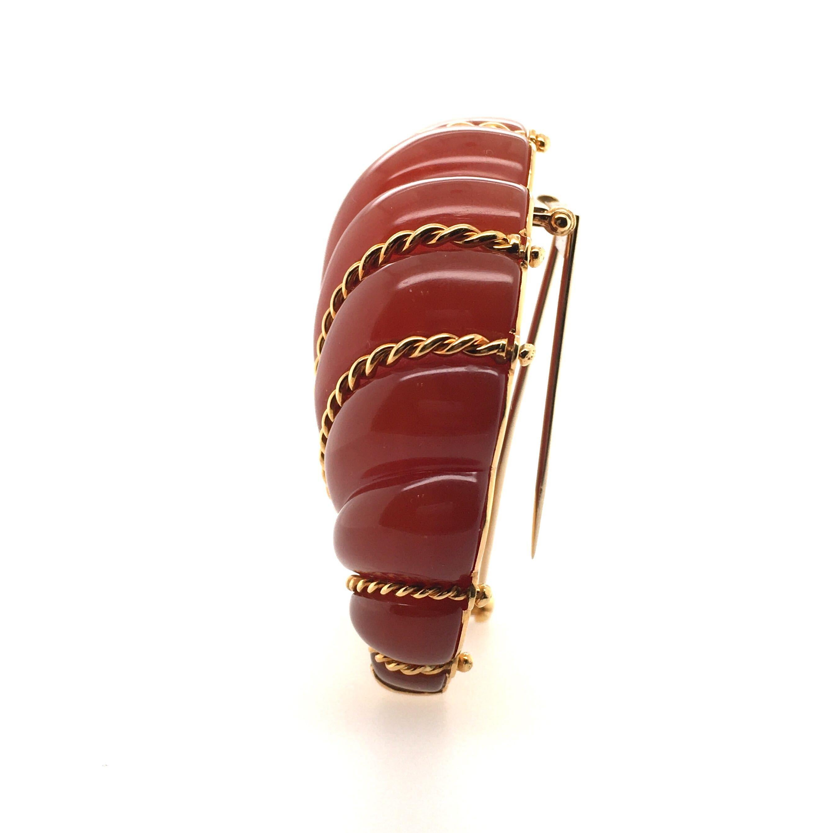 An 18 karat yellow gold and carnelian Fan brooch. Seaman Schepps. Designed as a carved carnelian fan shaped plaque, enhanced by gold ropework detail. The brooch measures approximately 2 1/2 x 1 inches, gross weight is approximately 67.3 grams.