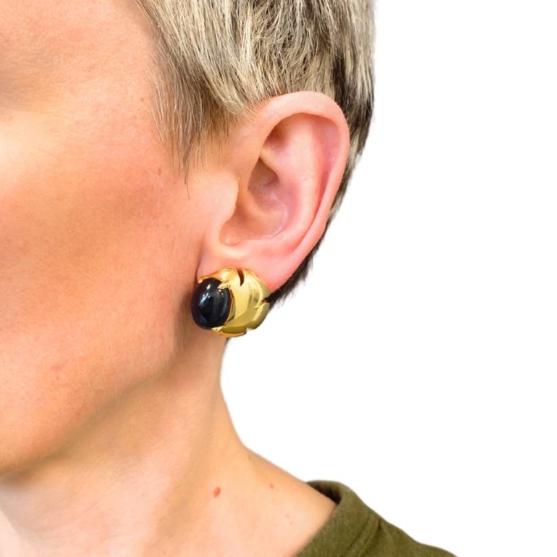 These exquisite Seaman Schepps earrings are masterfully crafted in 18k gold, showcasing the brand's signature bold and organic design. Each earring features a striking cabochon-cut gemstone—one a deep blue sapphire and the other a vibrant