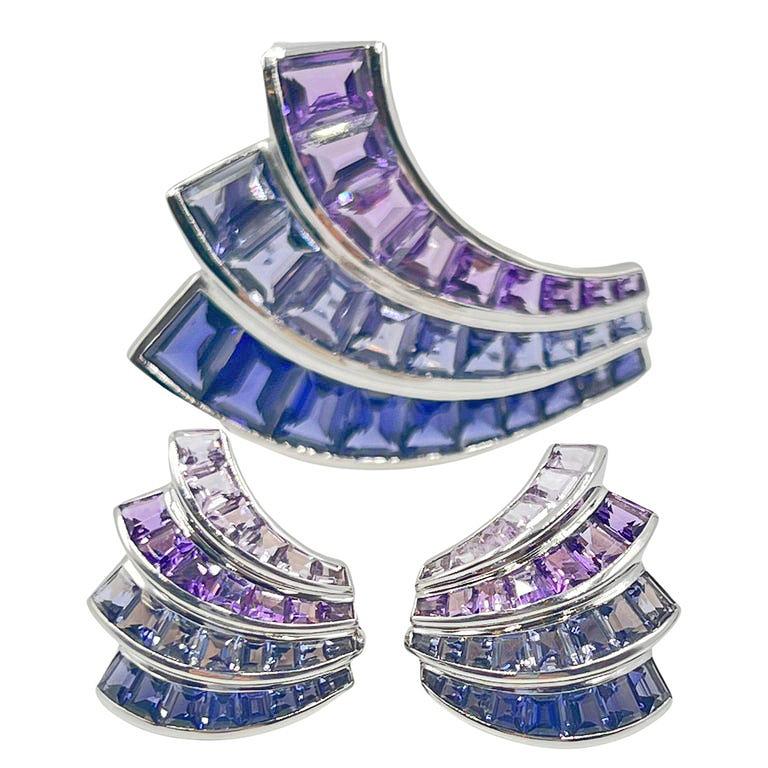 Seaman Schepps 18k white gold fan shaped brooch and earring three piece set.  Art Deco inspiration with shades of violet and blue tones in the iolite and amethyst fancy-cut gemstones. The brooch has a triple row of channel set, graduated amethyst