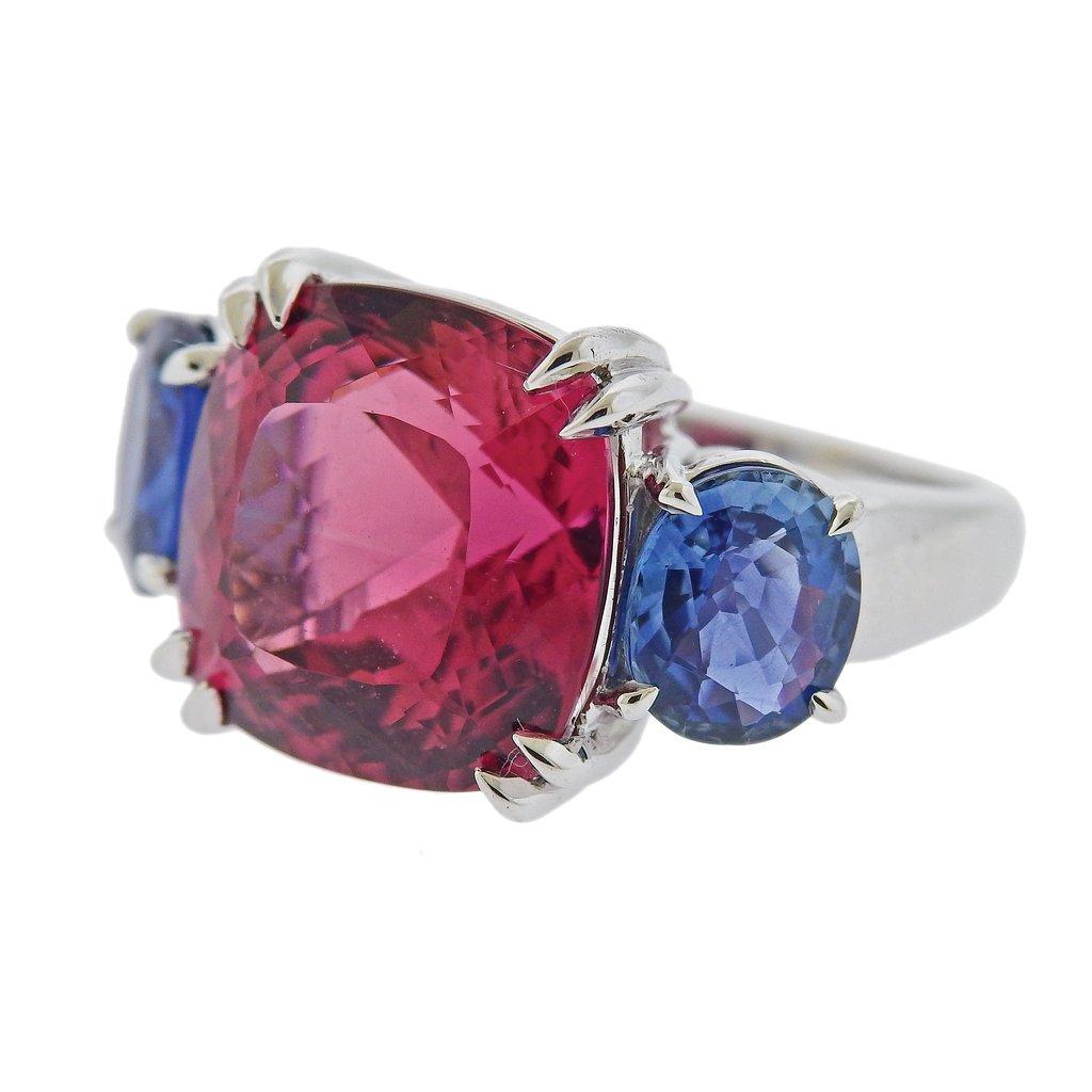 18k white gold ring by Seaman Schepps, set with approx. 15ct pink tourmaline, measuring 14.5mm x 14.6mm, and two oval sapphires on sides - approx. 8.3mm x 7.2mm and 8.5mm x 7mm. Ring size - 6.5, ring top - 14.5mm x 25mm. Weight is 13.6 grams. Marked