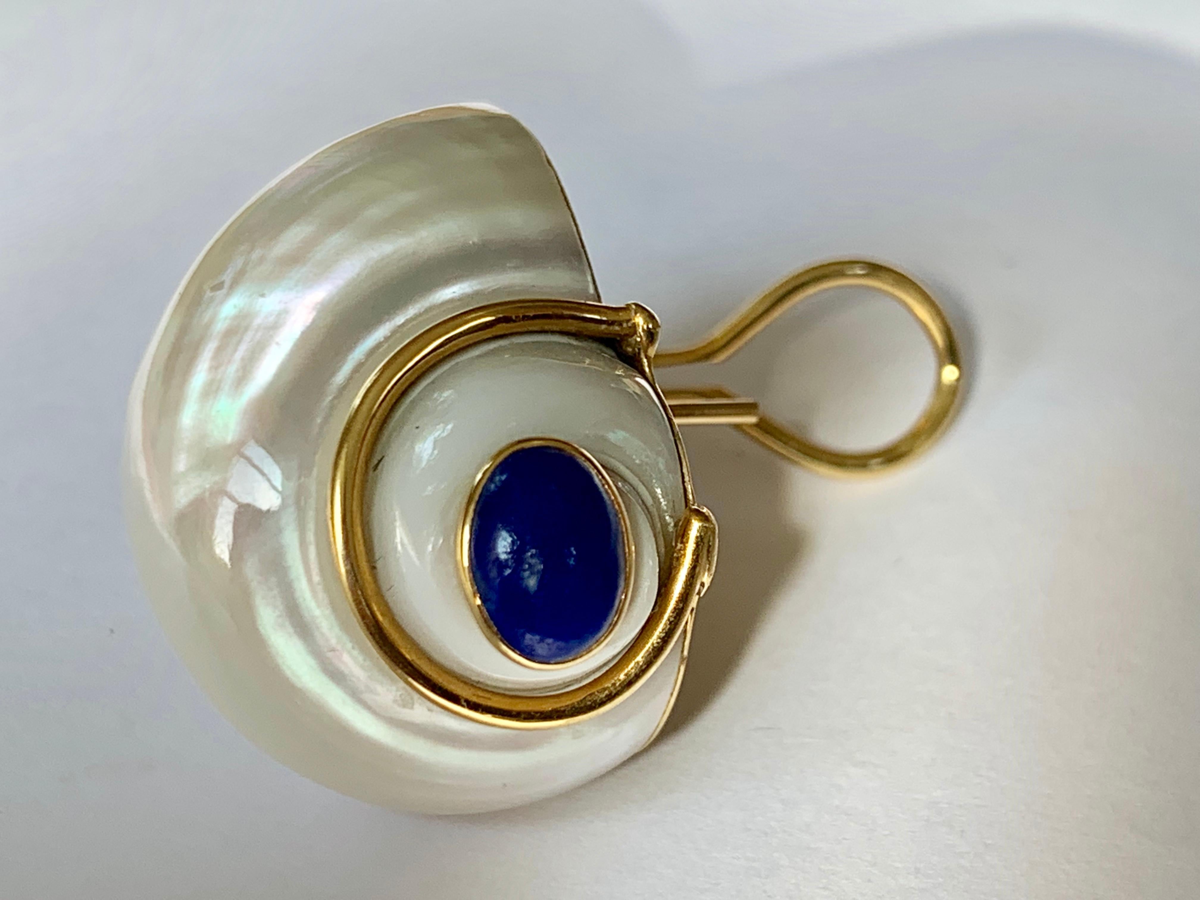 From Seaman Scheps, a pair of 18 karat yellow gold, turbo shell and Lapis Lazuli earrings. Each set with a white turbo shell, terminating in a Lapis Lazuli cabochon accented by gold wire. One shell has a little damage.