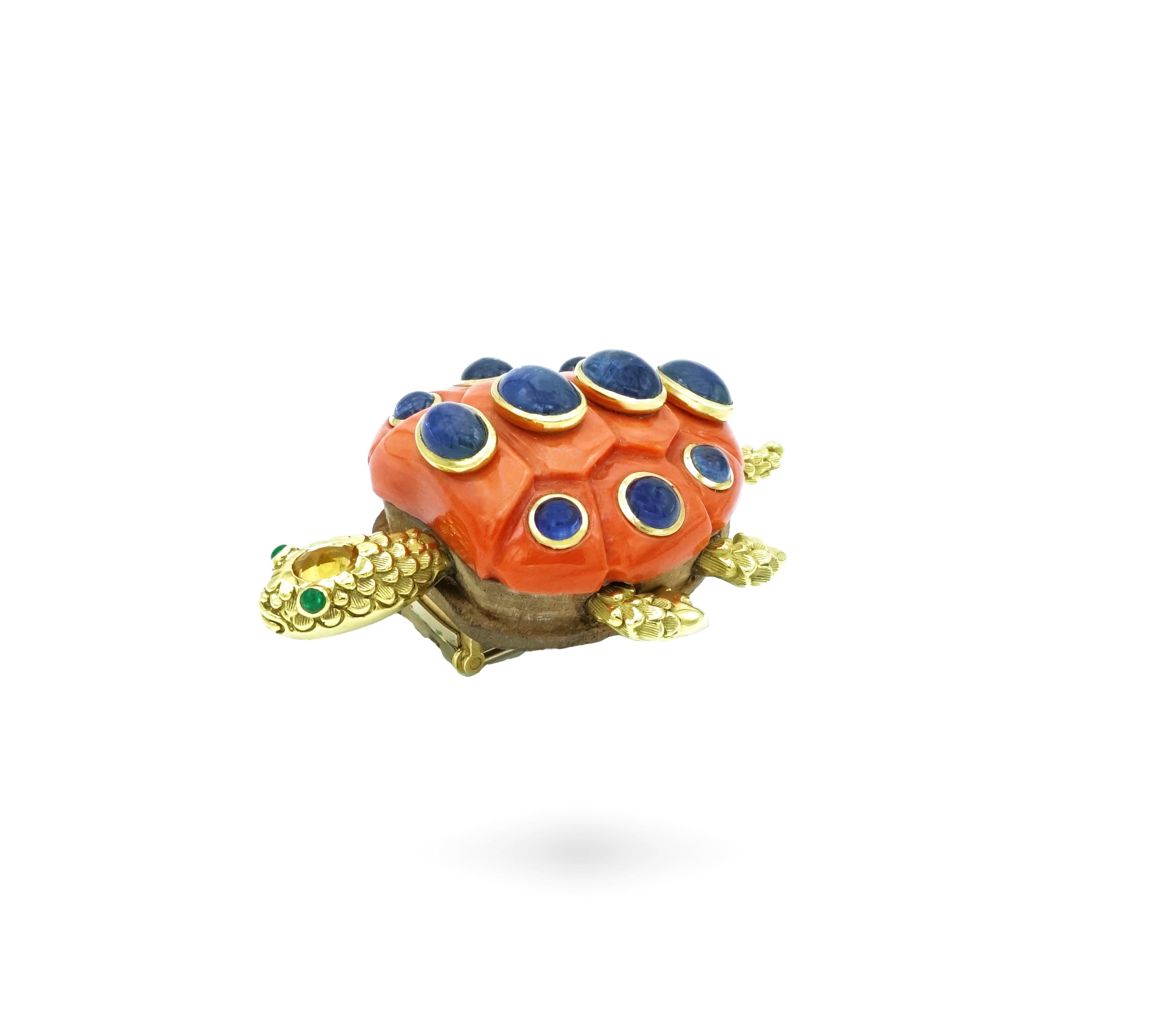 Seaman Schepps Brooch representing a title in yellow gold, the shell in coral set with cabochon sapphires, yellow sapphire, the eyes set with emeralds, and wood. 
Signed. 
Made in the 70'. 
29,75 grs