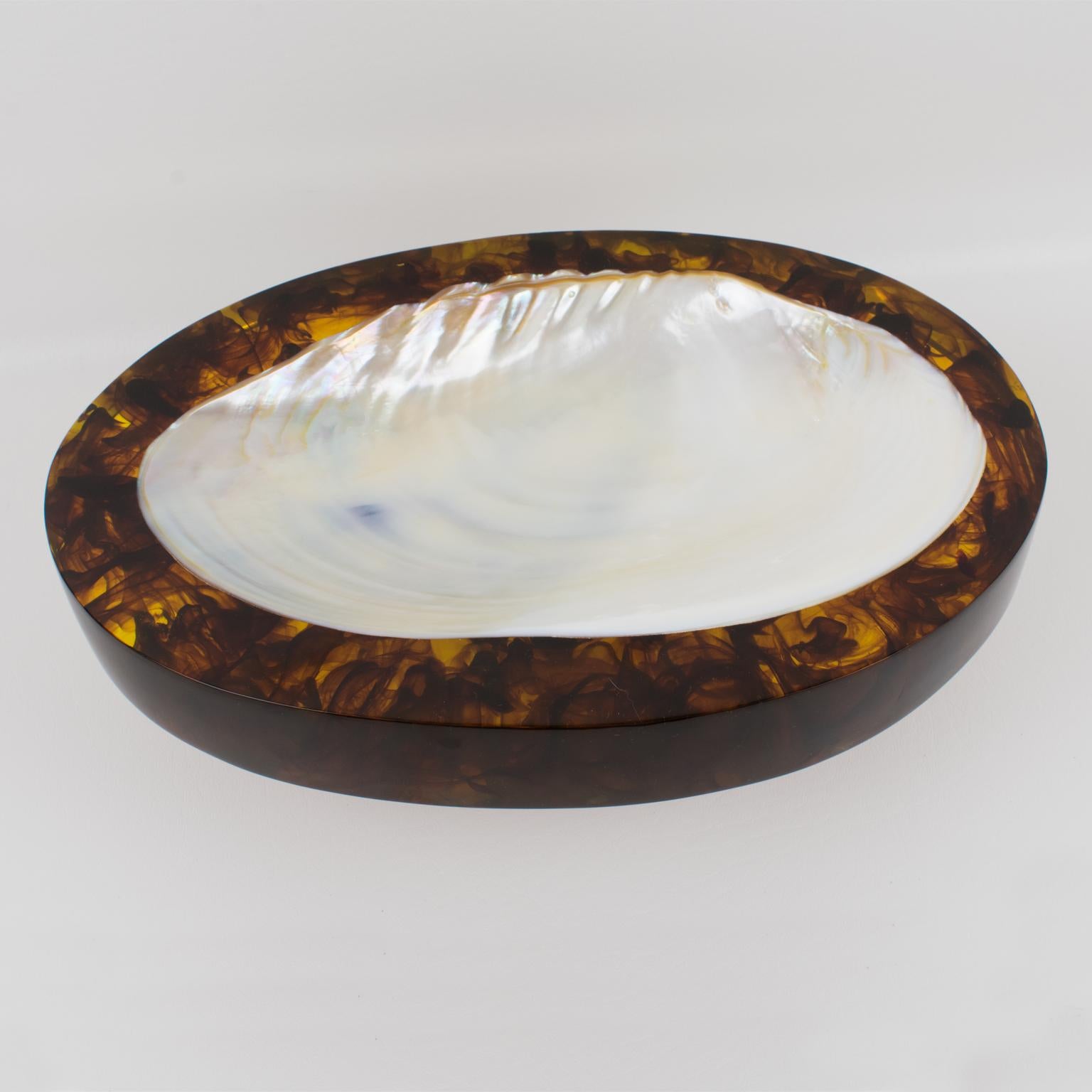 This stunning 1980s French modern desk tidy, vide poche, or catchall features an oval shape with an extra thick resin slab in a gorgeous rootbeer swirl color with a large seashell insert. There is no visible maker's mark.
The vide poche is in