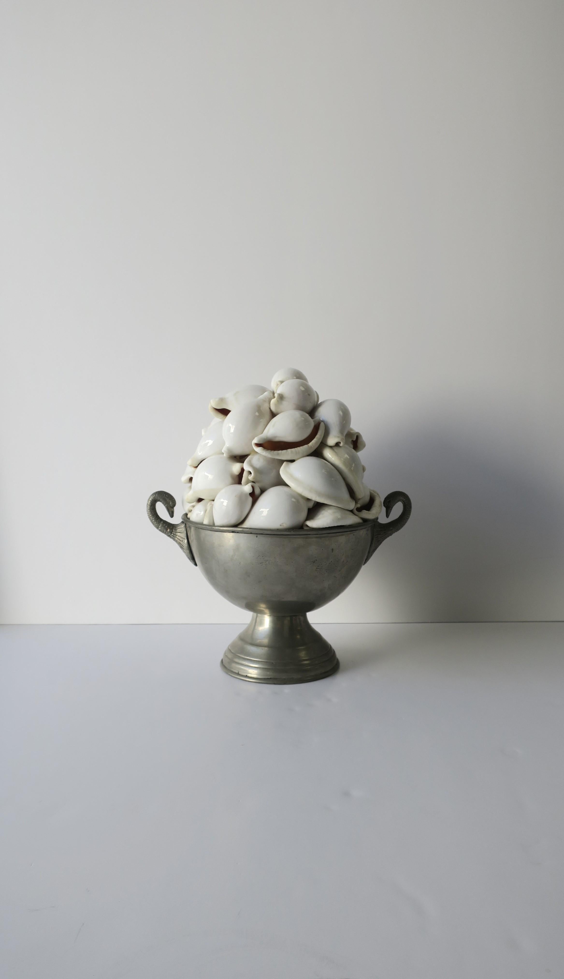 A beautiful seashell and urn sculpture piece decorative object, circa early-20th century. Piece/sculpture 'topiary' has a metal urn base with bird handle design, filled with white seashells (shells are attached to one-another and attached to urn,