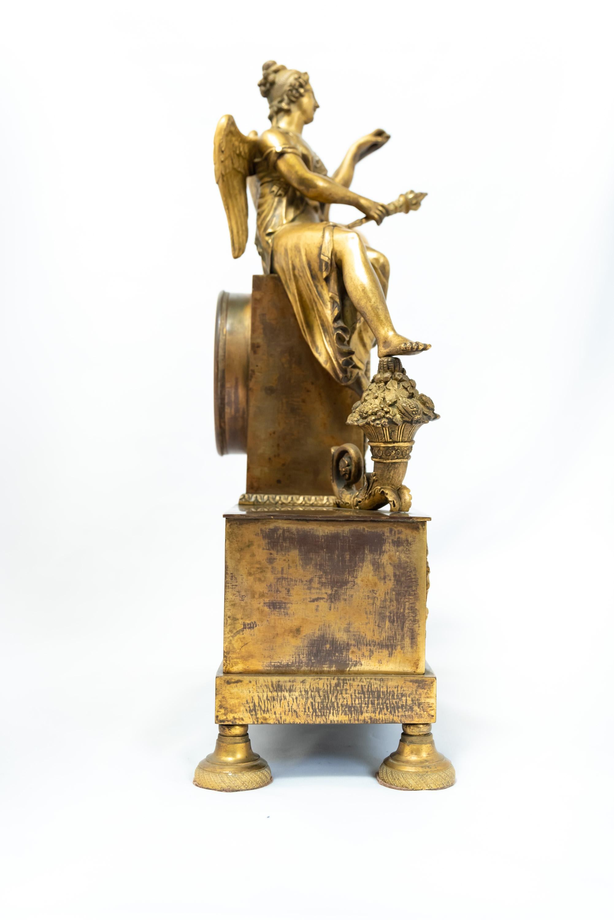 A French fire-gilt clock depicting a seated female figure - Urania, I presume, judging from the iconography. Empire Era, 1800-1815. The gilding shows signs of wear, and the silvered silk-thread mechanism is in unverified condition.