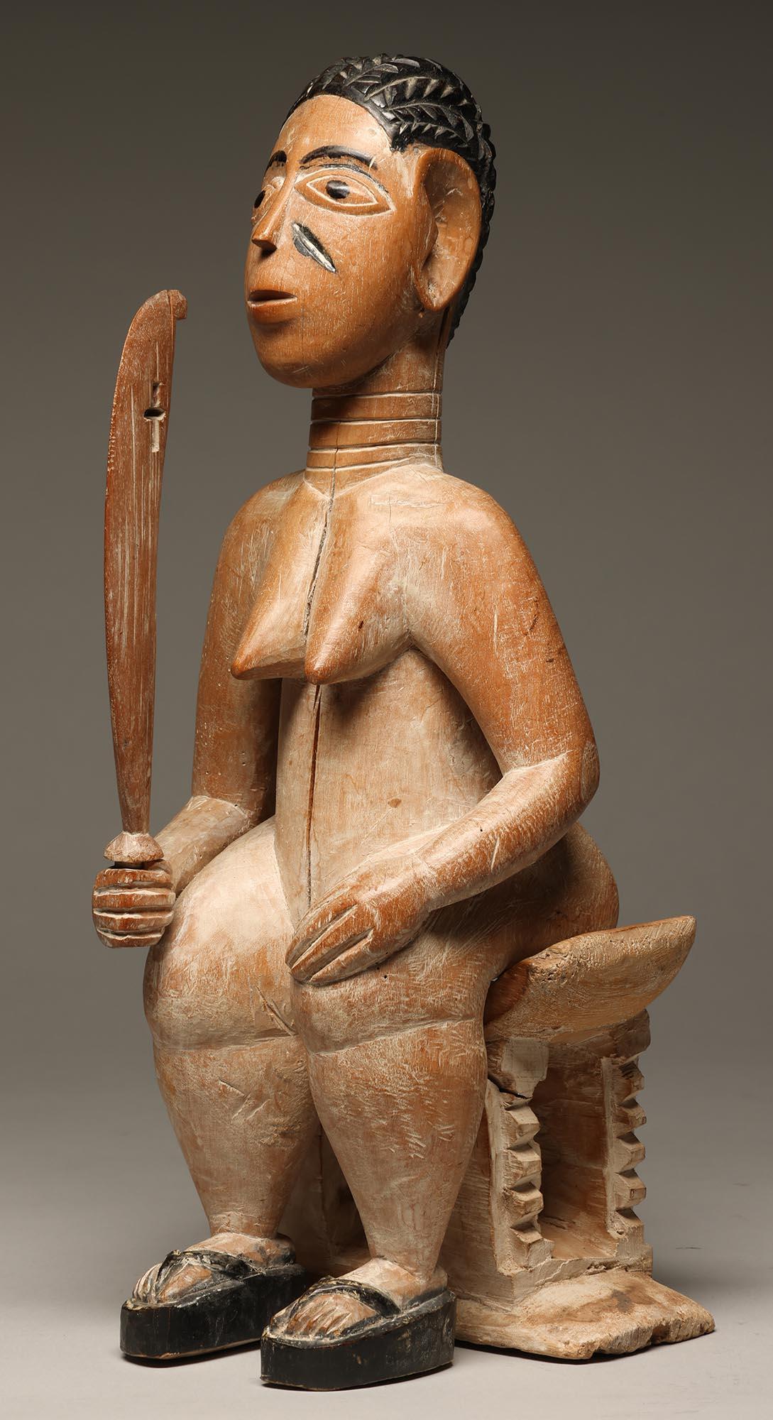 Figure féminine assise sur un tabouret Akan classique, tenant une épée.  Provenant du peuple Ewe du Ghana, Afrique de l'Ouest. Créée en trois pièces distinctes qui s'emboîtent pour l'exposition, la figurine, le tabouret et l'épée. Traces de blanc,