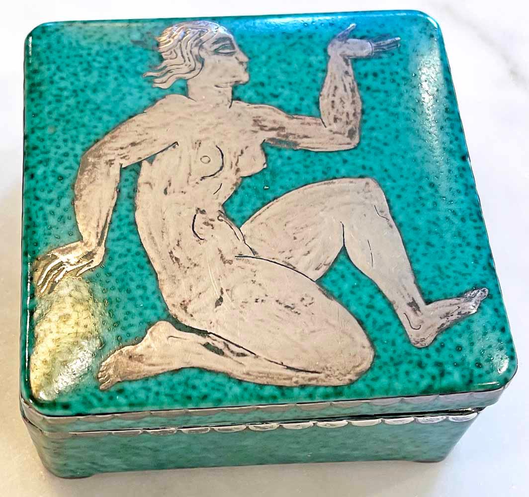 This lovely Art Deco box features a greenish-turquoise glaze with silver overlay depicting a seated female nude on the cover, and a silvered grid inside.  This is a fine example of the Argenta line of ceramics created by Wilhelm Kåge, artistic