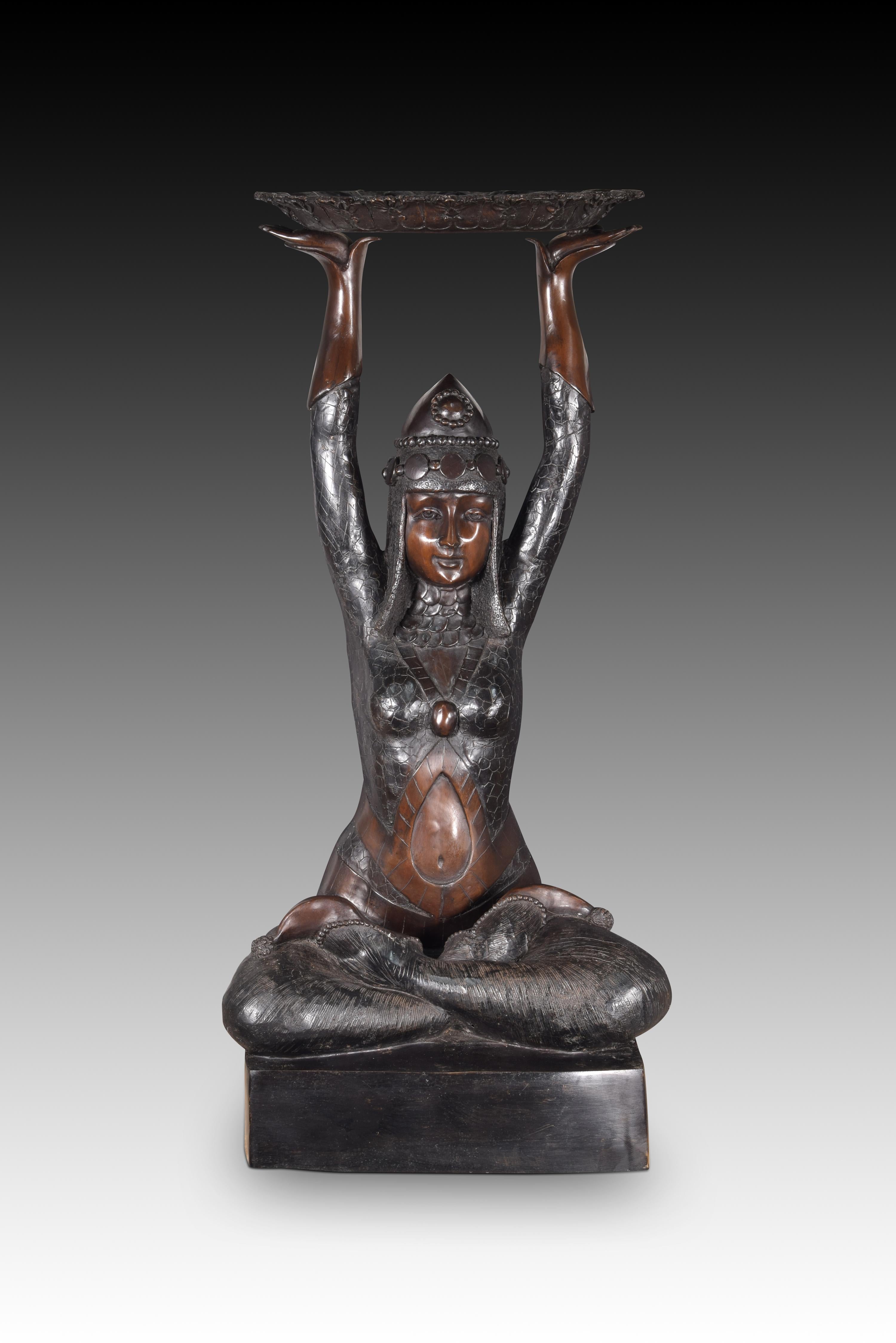 Seated offeror. Bronze. 20th century, following Art Deco models. 
Bronze sculpture of a young lady sitting with her feet crossed and raising both arms to hold aloft an oval tray. Her clothing (exotic, detailed, marking the figure...) and the posture