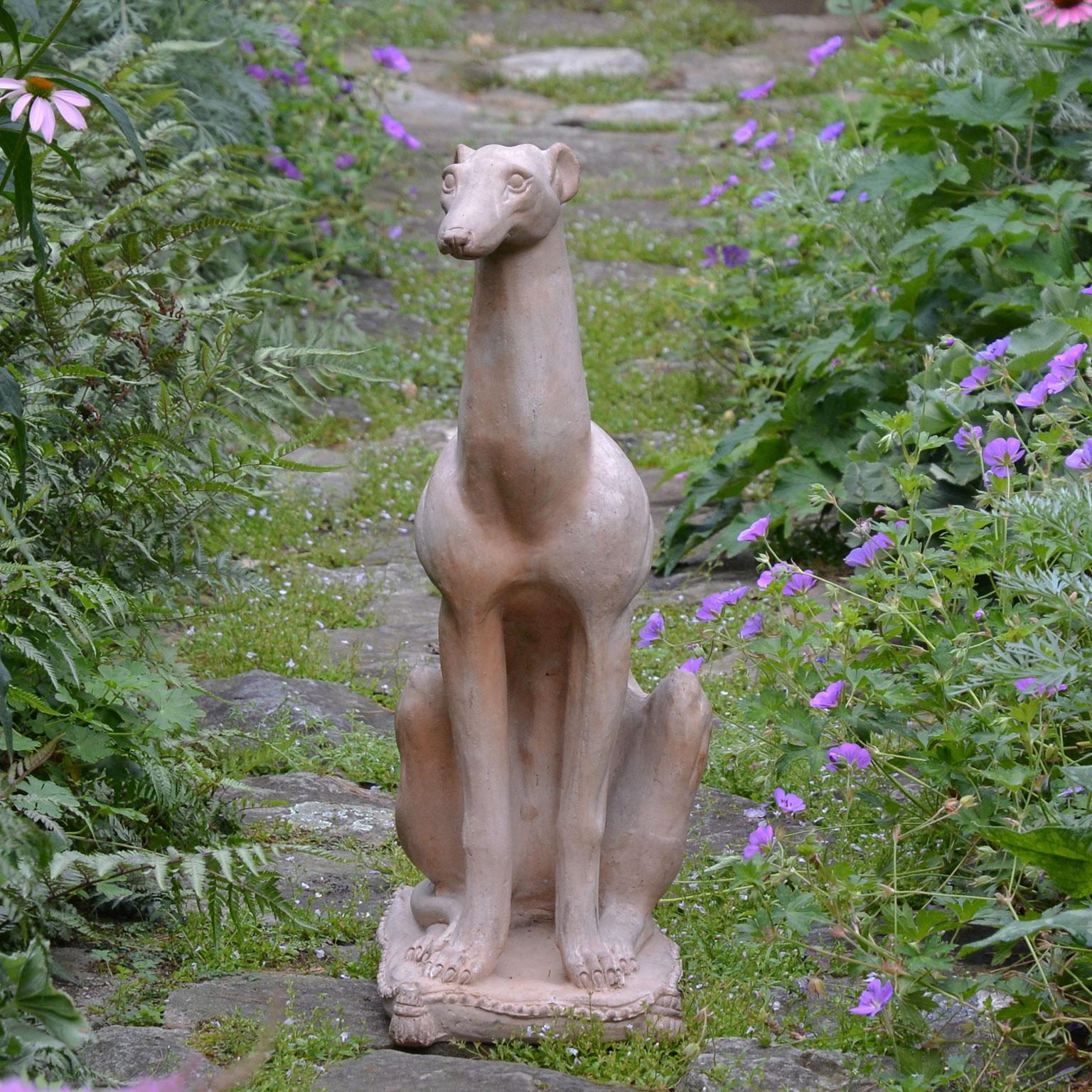 A terracotta figure of a seated whippet, of stylized Art Moderne form with articulated musculature, seated on a tasseled pillow, English, circa 1930. Measures: 26 ins. high, 9 ins. wide, 13 ins. deep.