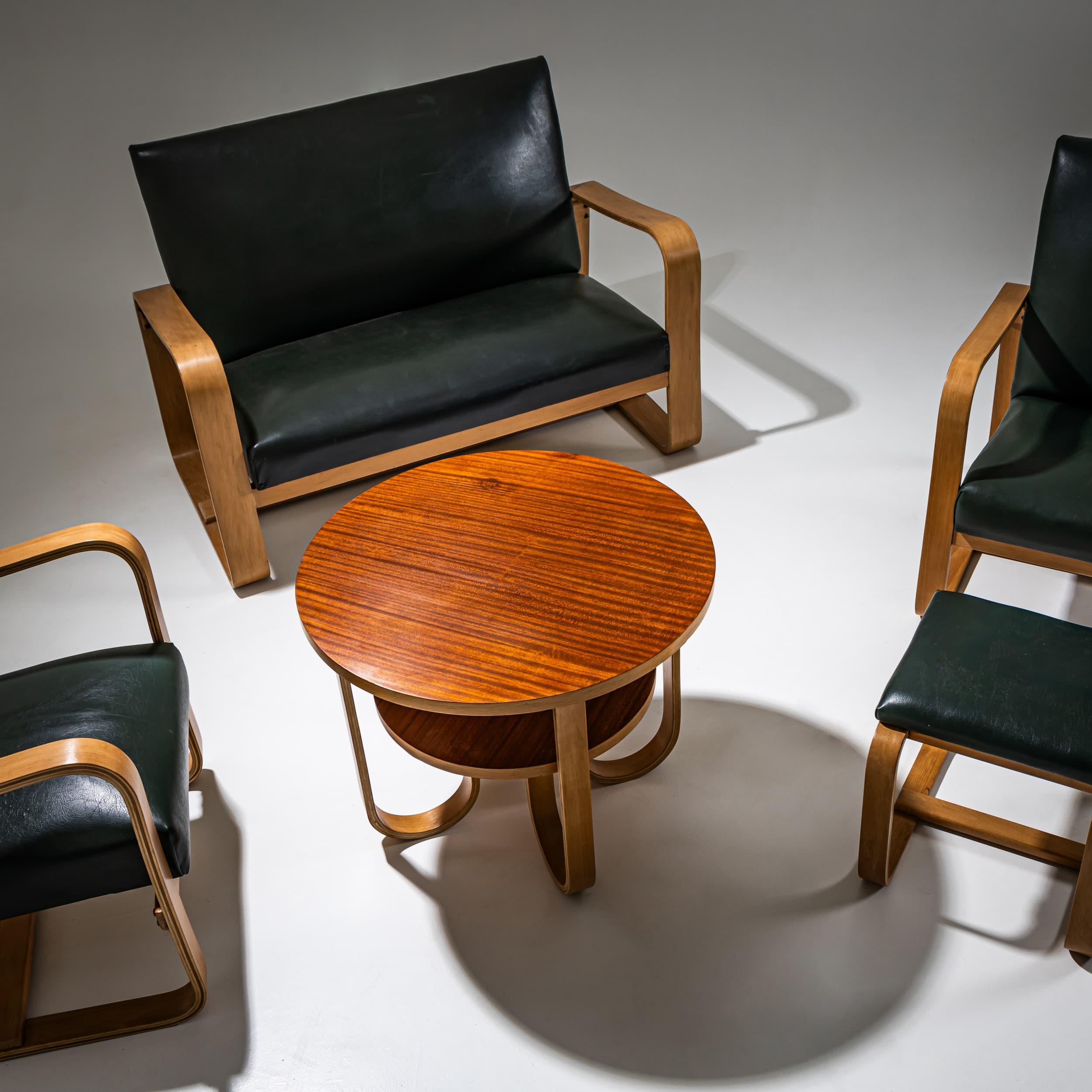 Un insieme di sedute composto da due poltrone, un divano a due posti, uno sgabello e un tavolino. I pezzi sono rivestiti in ecopelle verde scuro, creando un raffinato contrasto con le strutture in legno chiaro.
Giuseppe Pagano Pogatschnig è stato un