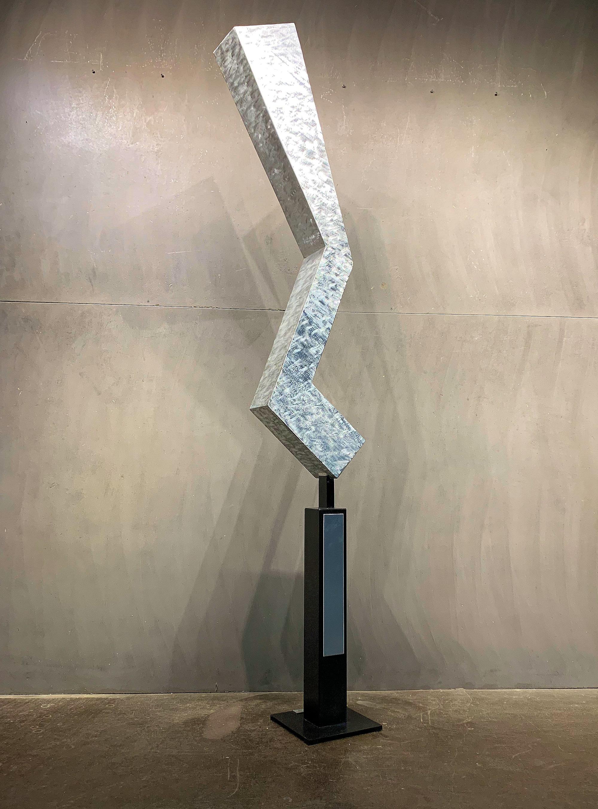 A hollow-body sculpture made from TIG welded aluminum, concrete and steel (base).  This design exhibits an overly exaggerated bending and falling beam.  In addition to the mood of the shape; selected bends have induced thermal cracks to portray