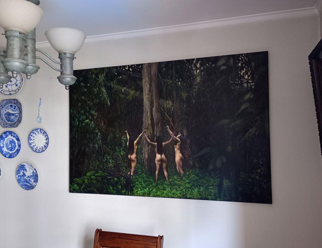 Das Kunstwerk zeigt eine eindringliche und faszinierende Szene, in der drei Figuren inmitten eines dichten, grünen Regenwaldes stehen. Die Personen, die mit dem Rücken zum Betrachter dargestellt sind, heben ihre Arme in Richtung eines hoch