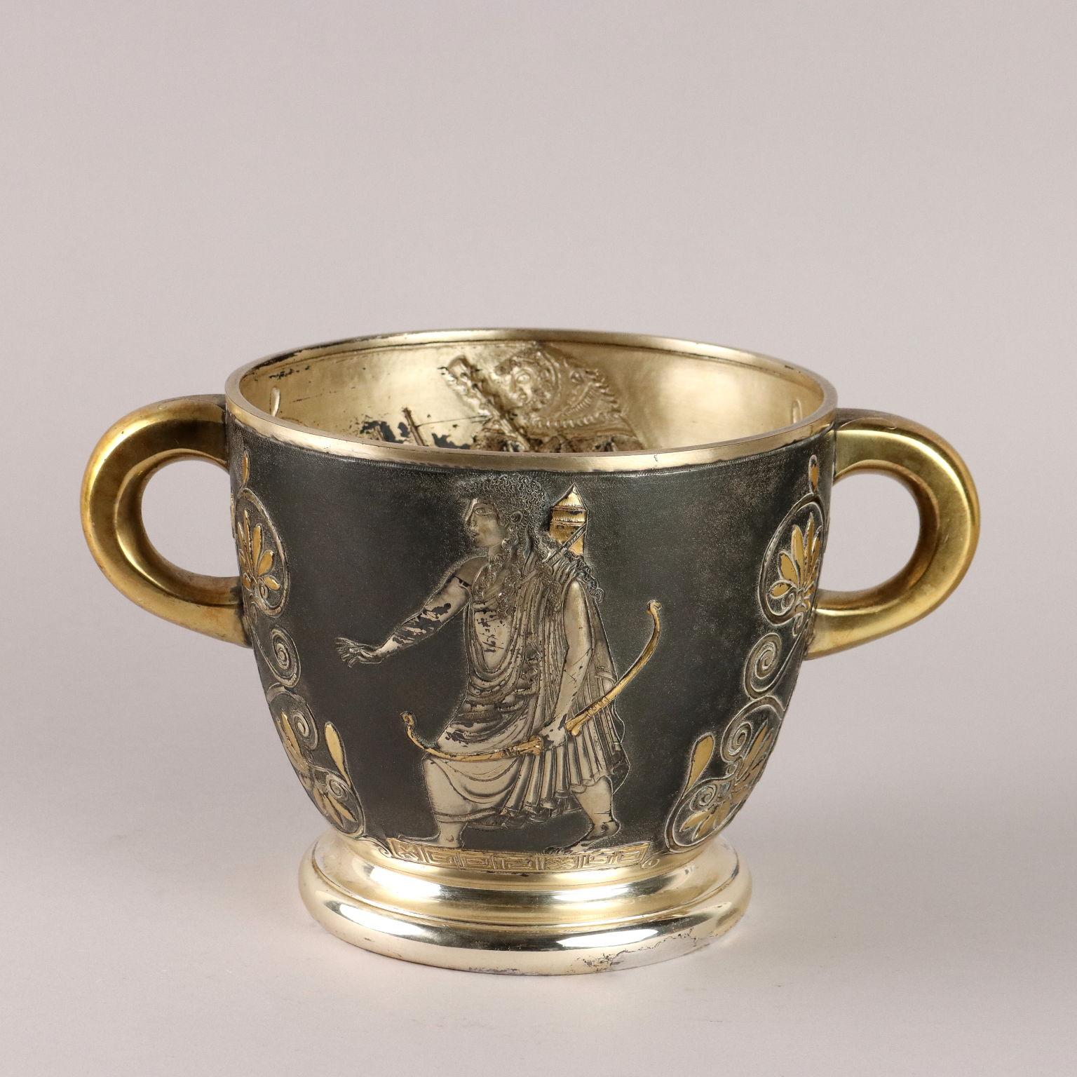 Secchiello in argento brunito finemente lavorato a bulino e sbalzato con parti dorate. Decoro con figure mitologiche e motivi vegetali attorno alle anse ad anello. Sotto la base marchi incussi dell'argento e dell'argentiere. Grammi 1130.