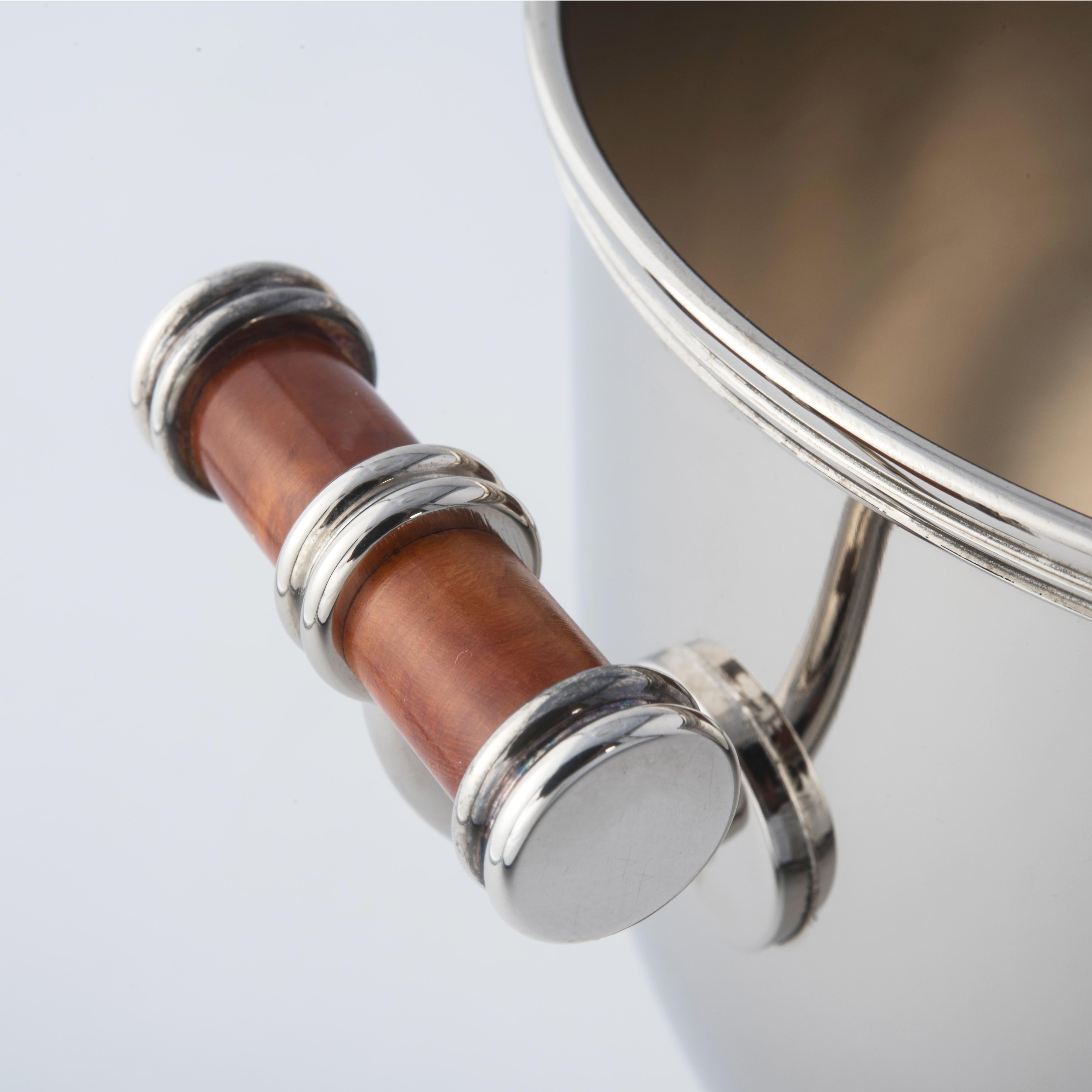 Verleihen Sie Ihrer Tafel einen Hauch von Eleganz mit dem Champagnerkübel Nino Basso. Sein raffiniertes Design mit der abgerundeten Tasse und den Griffen aus Heidekraut mit gestreiften Endringen macht ihn zu einem exklusiven Accessoire für