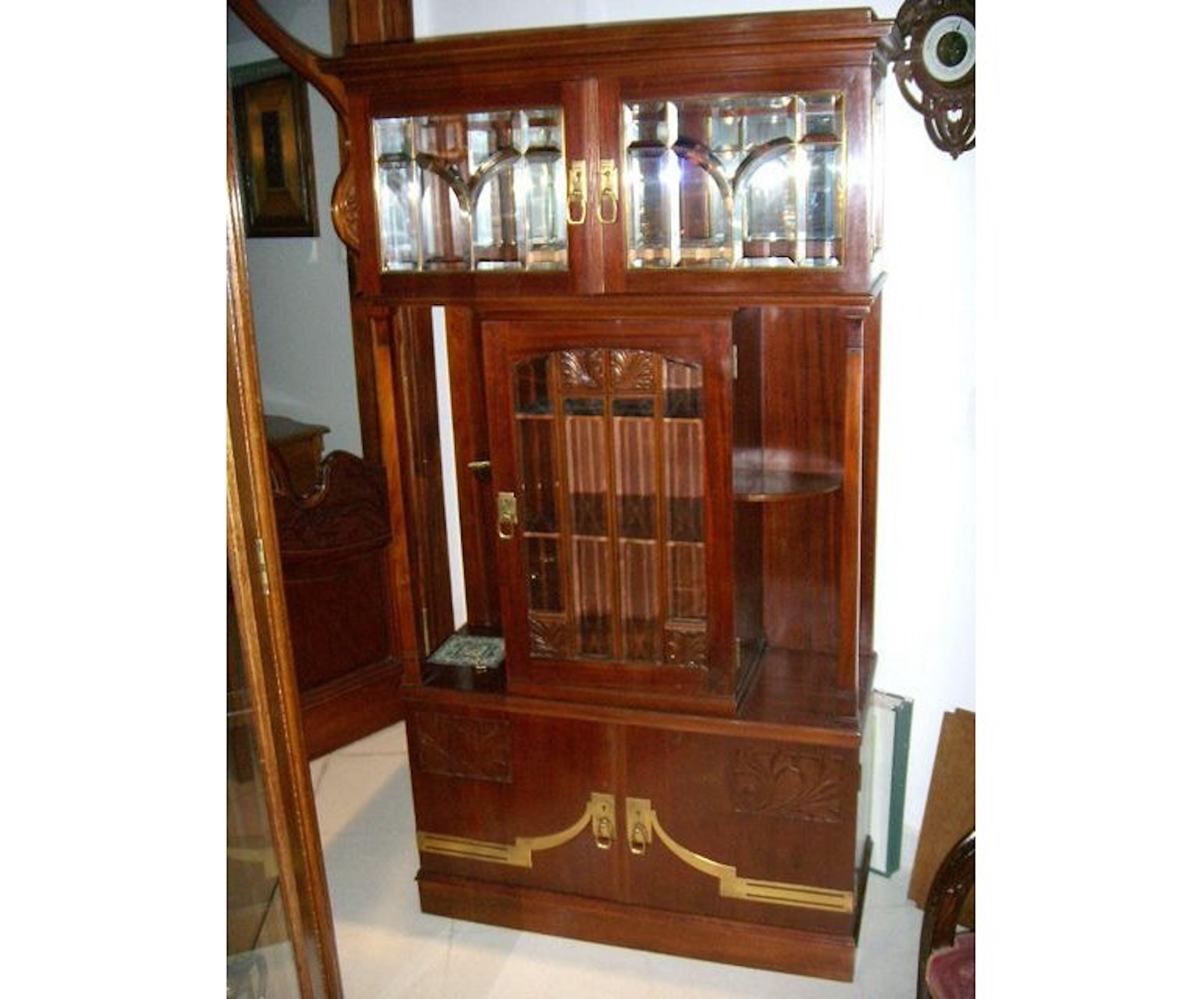 A Secessionist style Arts and Crafts mahogany display cabinet with two upper beveled glass doors, and a central display cabinet with stylised floral carvings above flanked by four open display shelves to each side with a double cupboard to the base,