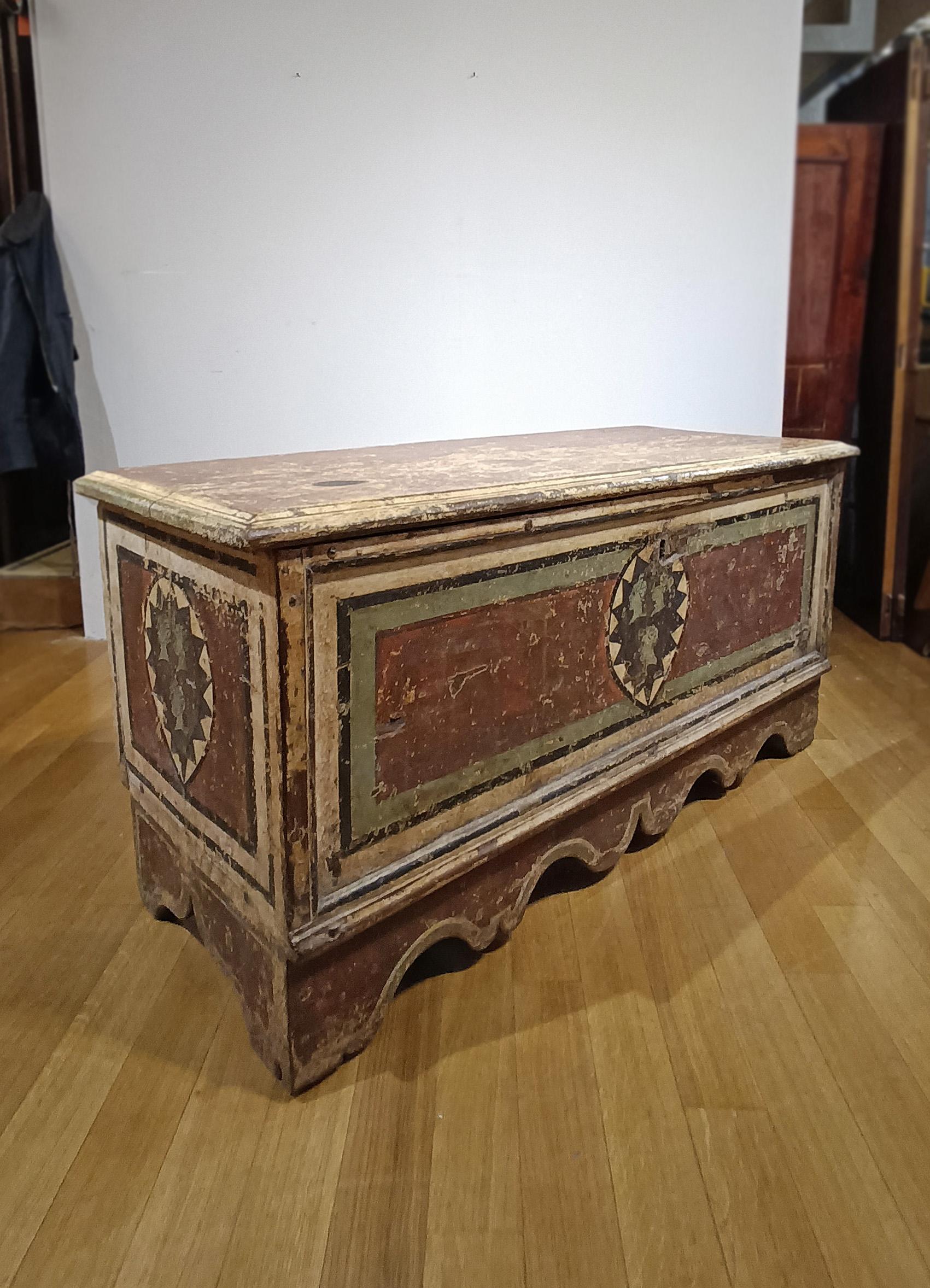 Elegante e unica cassapanca in legno massiccio di castagno, dipinta a tempera nei toni del rosso, verde, giallo e nero. La cassapanca è di forma rettangolare, con piedi a mensola e un piano sporgente. Il suo interno spazioso presenta anche un