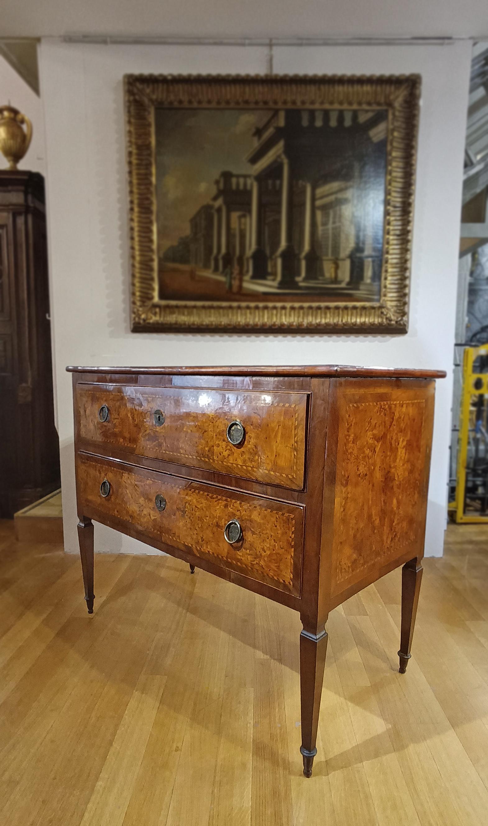 Elegant chest of drawers veneered in poplar and walnut burl. The front, sides, and top feature geometric inlays, creating frames and adding further refinement. The chest of drawers features truncated pyramid legs typical of the Neoclassical period,