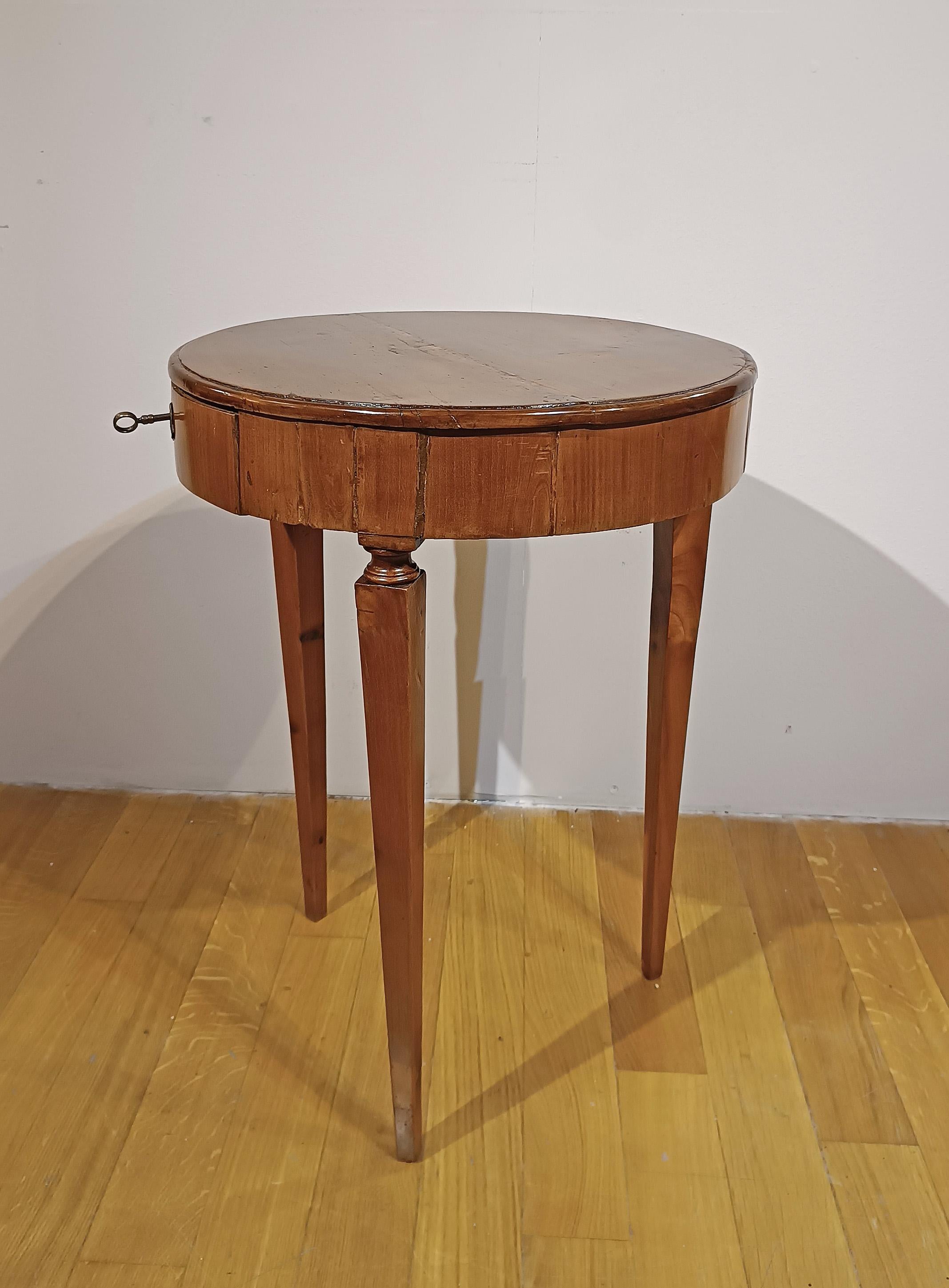 Raffinato tavolino da caffè impiallacciato in noce, finemente intagliato. Il pezzo presenta tre gambe tronco-piramidali, tipiche dell'epoca, e un piano con una fascia circolare. Il tavolo è dotato di un piccolo cassetto, pratico per riporre piccoli