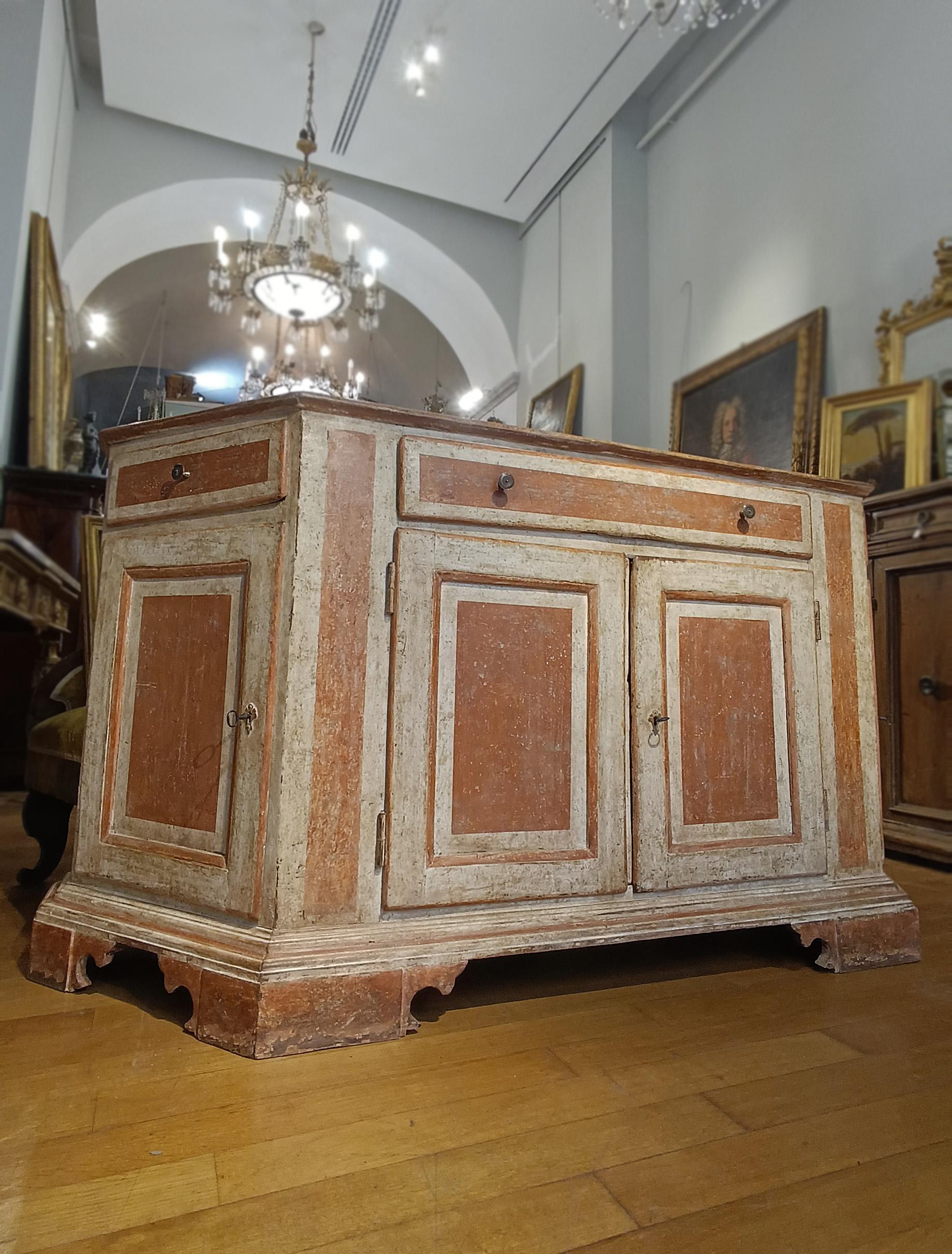 Elegantes Sideboard aus Tannenholz, geschnitzt und mit magerer Temperamalerei in einem raffinierten Zweifarbenton aus Weiß und Rotbraun bemalt. Die geometrischen Motive des Gemäldes unterstreichen die Form des Möbelstücks und verleihen ihm einen
