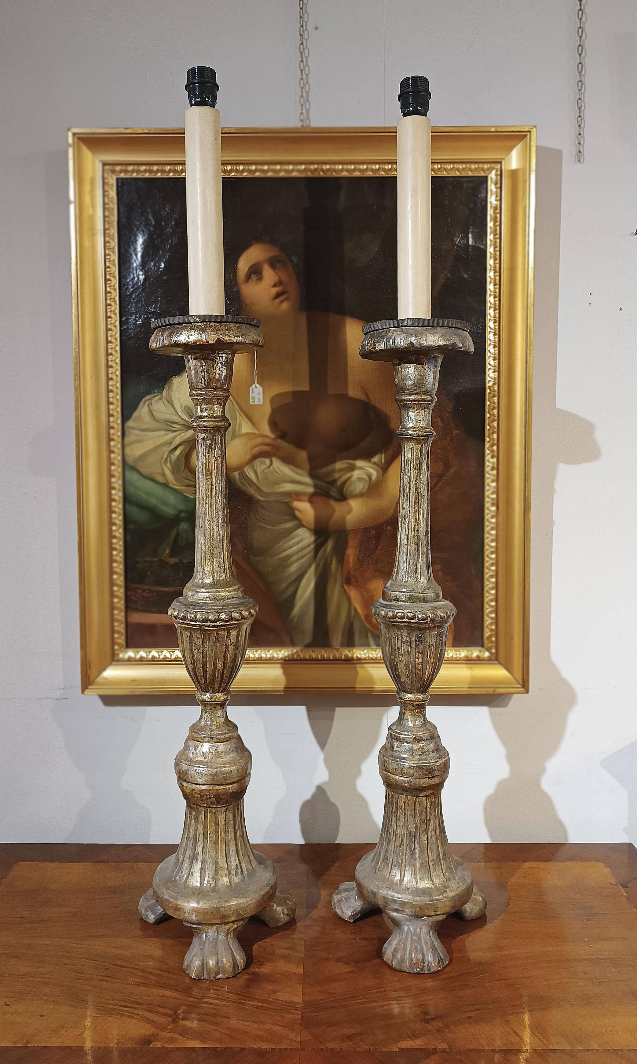 Encantadora pareja de candelabros de madera finamente tallada y acabados en pan de plata. Estos candelabros se distinguen por su fuste elegantemente tallado, enriquecido con delicadas estrías, y por la base sostenida por tres patas ferales. En la