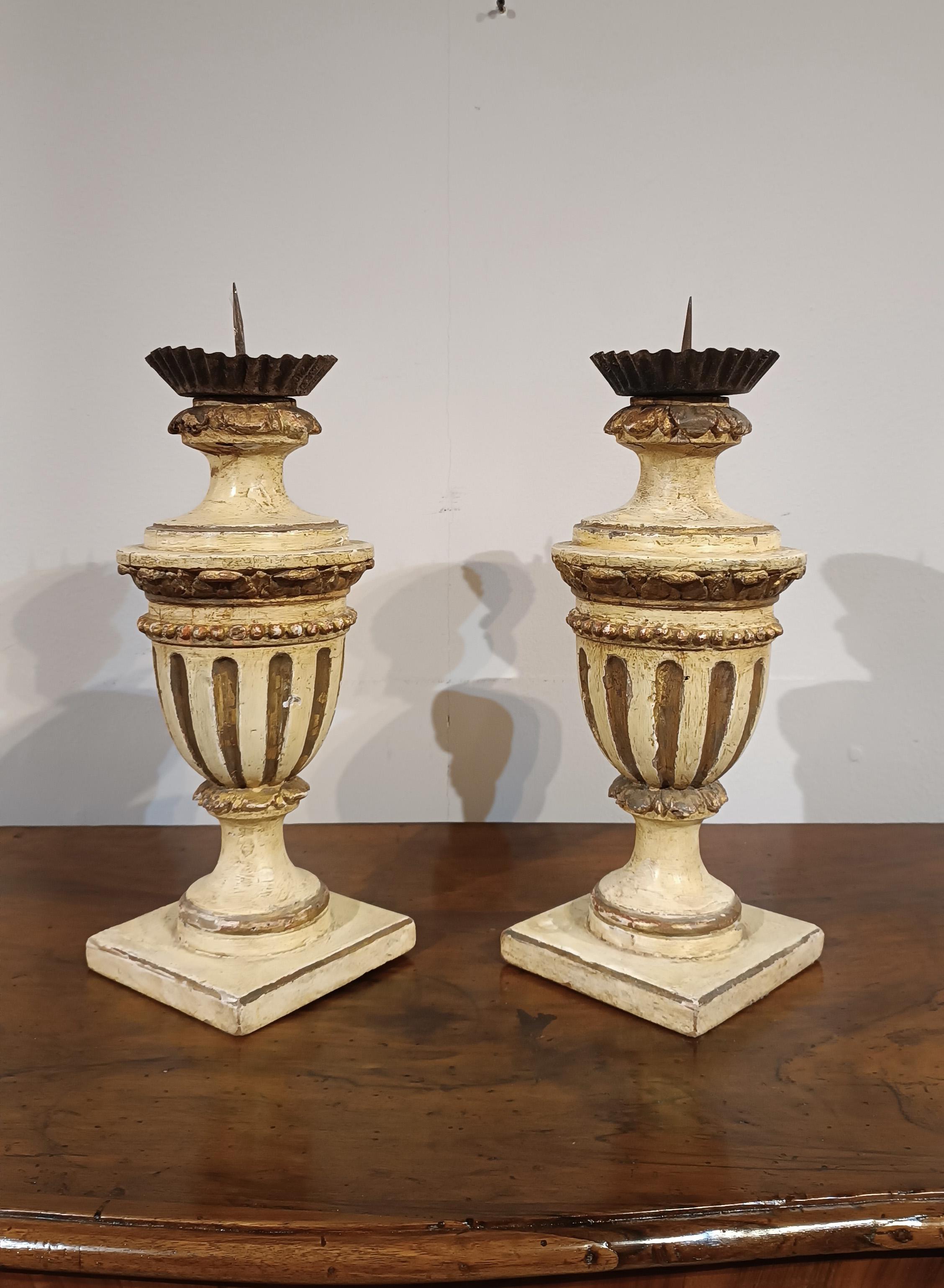 Elegant pair of carved and ivory-lacquered Swiss pine candelabra, embellished with pure gold trim. The candelabra have a square base and a smooth amphora shape, enhanced by refined details. The gilded decorations lend a touch of class and superior