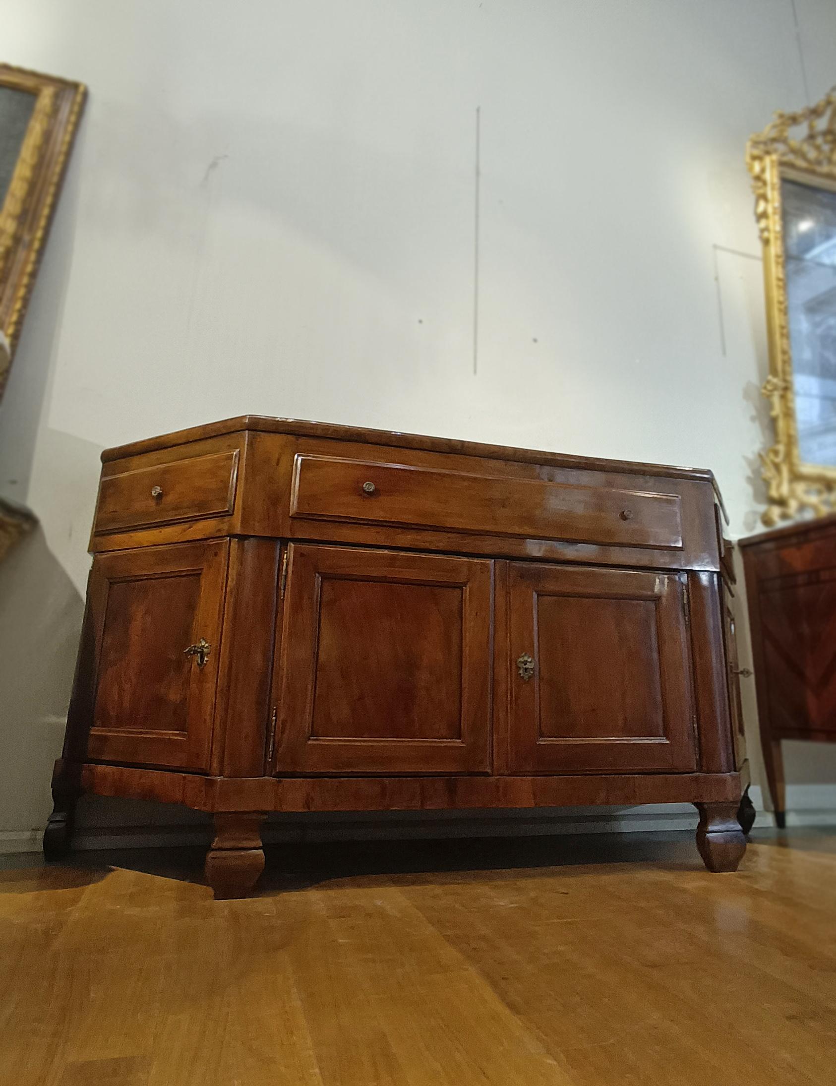 Beautiful sideboard in solid and veneered walnut, hand-carved. The sideboard has a rounded shape, with a smooth top that protrudes slightly and a base characterized by truncated pyramid feet. It is composed of three drawers and four doors, arranged