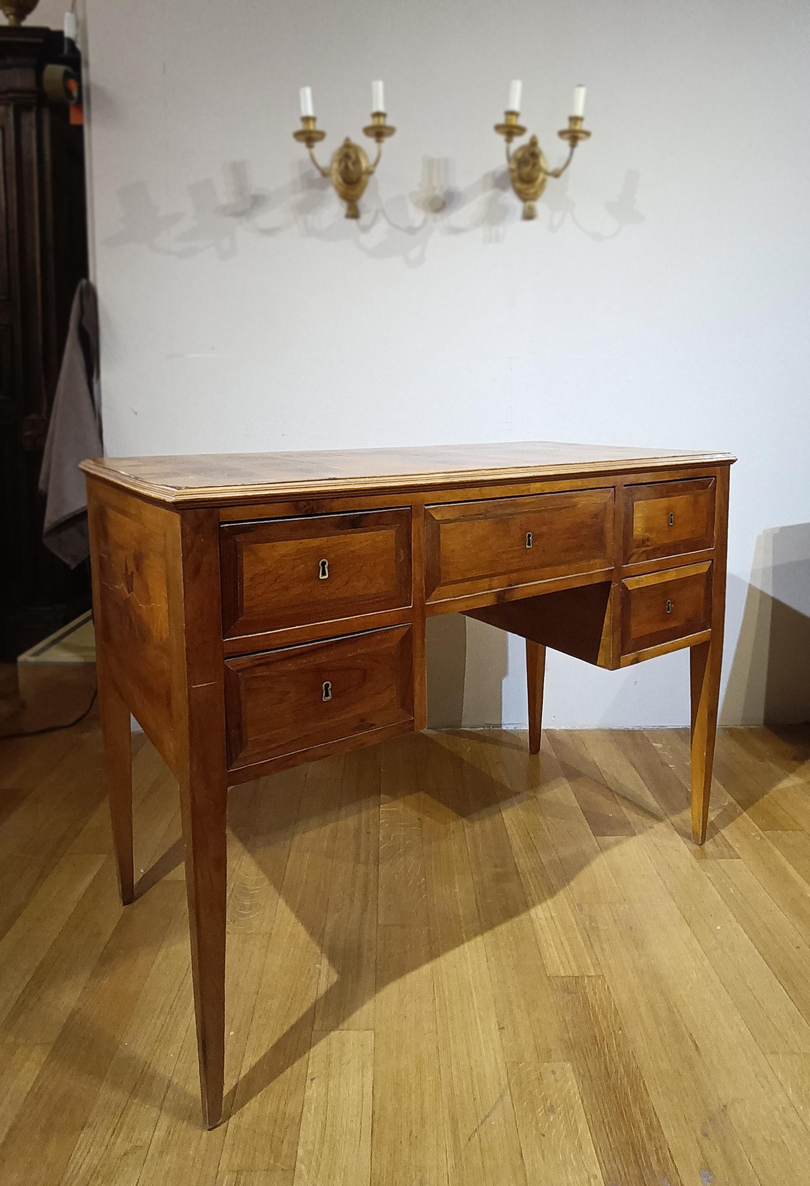 Elegant small veneered writing desk in walnut and olive wood, finely carved. The writing desk is distinguished by its truncated pyramid legs, typical of the period, and features refined inlays on both the front and the top, centered on a star, with