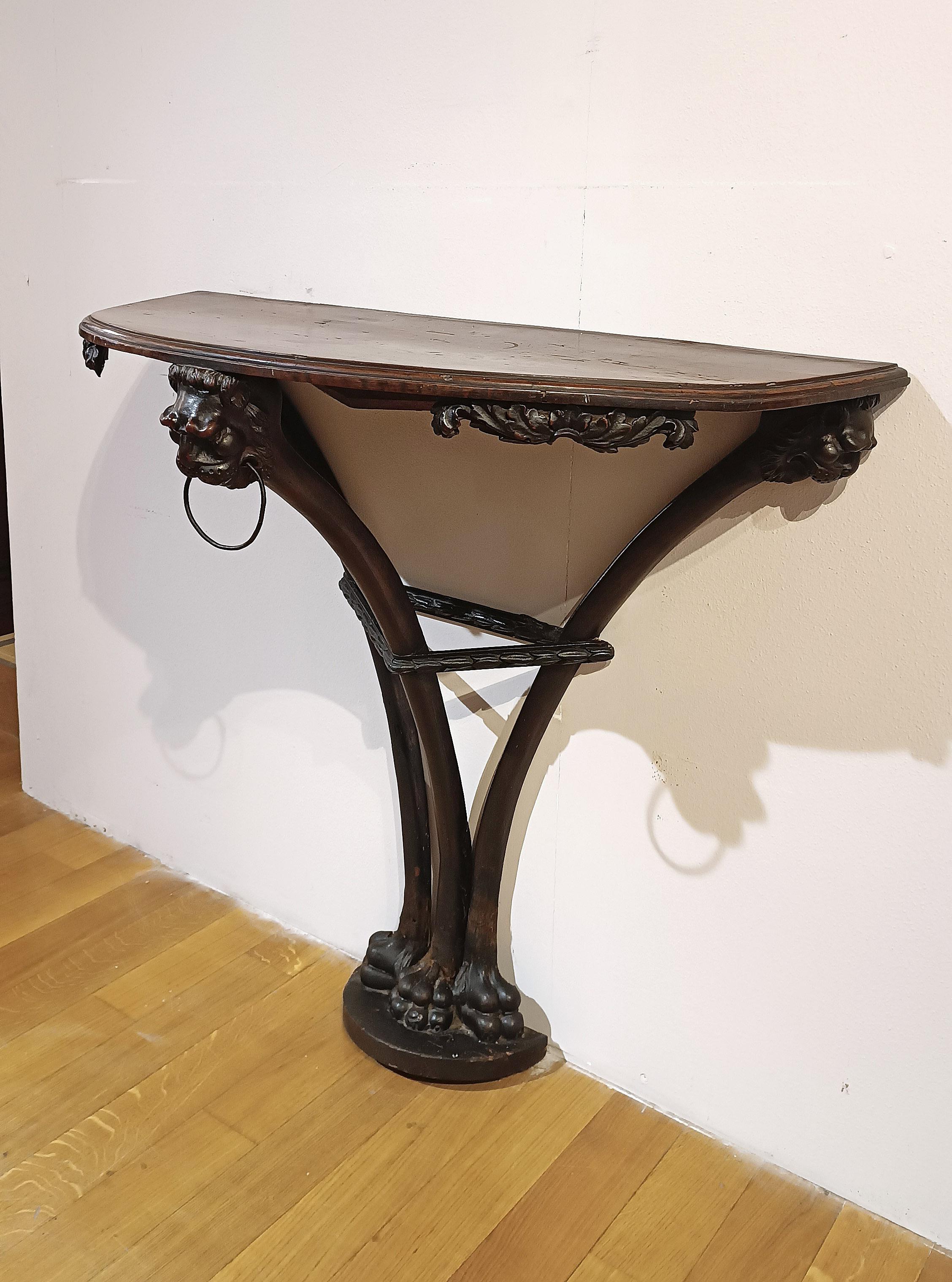 Elegant, finely carved solid walnut consolle table. The consolle table features a crescent-shaped top and three feral legs. It is decorated with geometric carvings, plant motifs, and lion heads at the corners and center, enhancing its refinement.