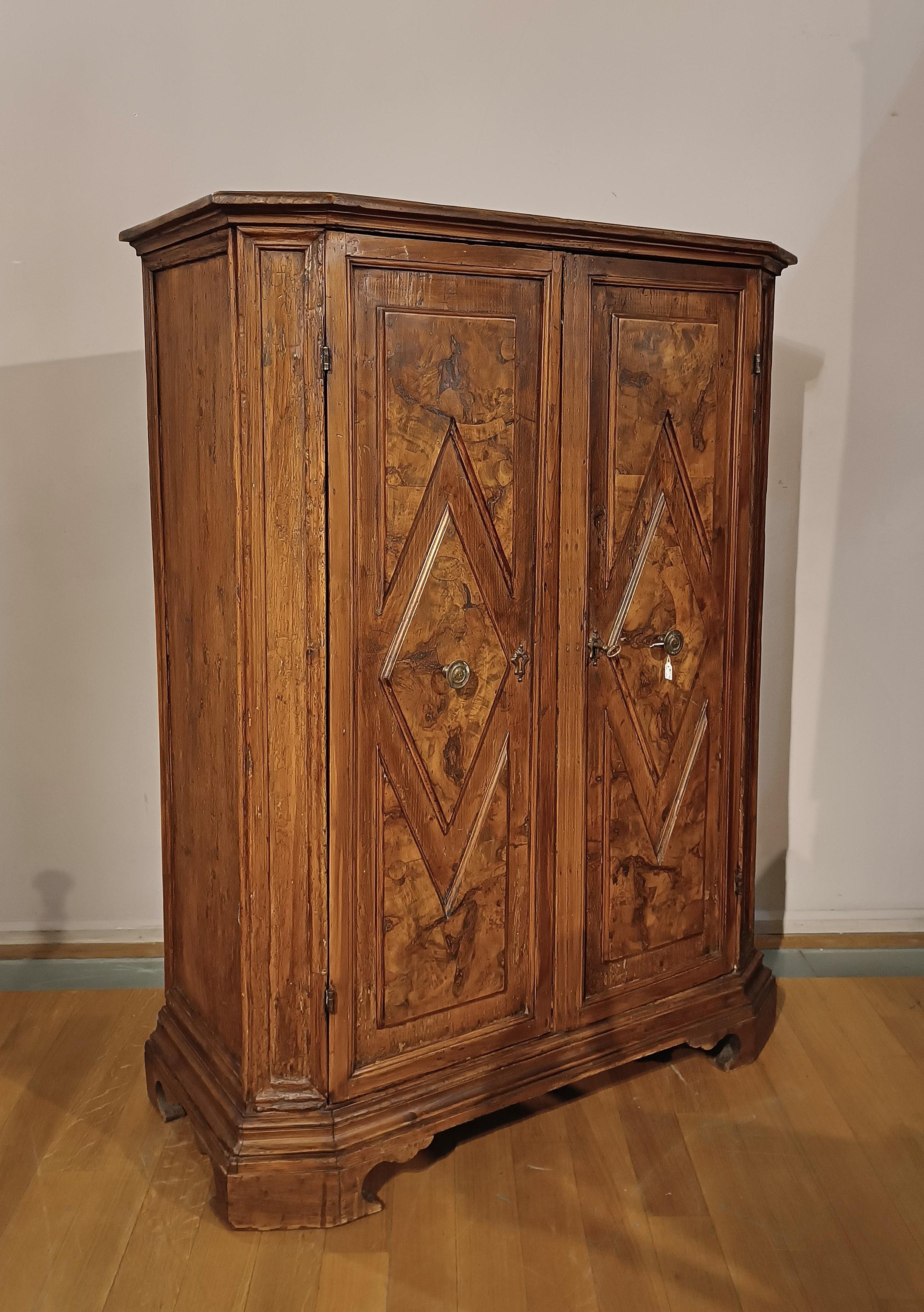 Beautiful cabinet with two doors in soft wood, with walnut briar tiles and blonde half-luster finish. The carved decoration is linear and geometric, visible both on the front and on the sides. The base is shelf-like, while the top is smooth with a