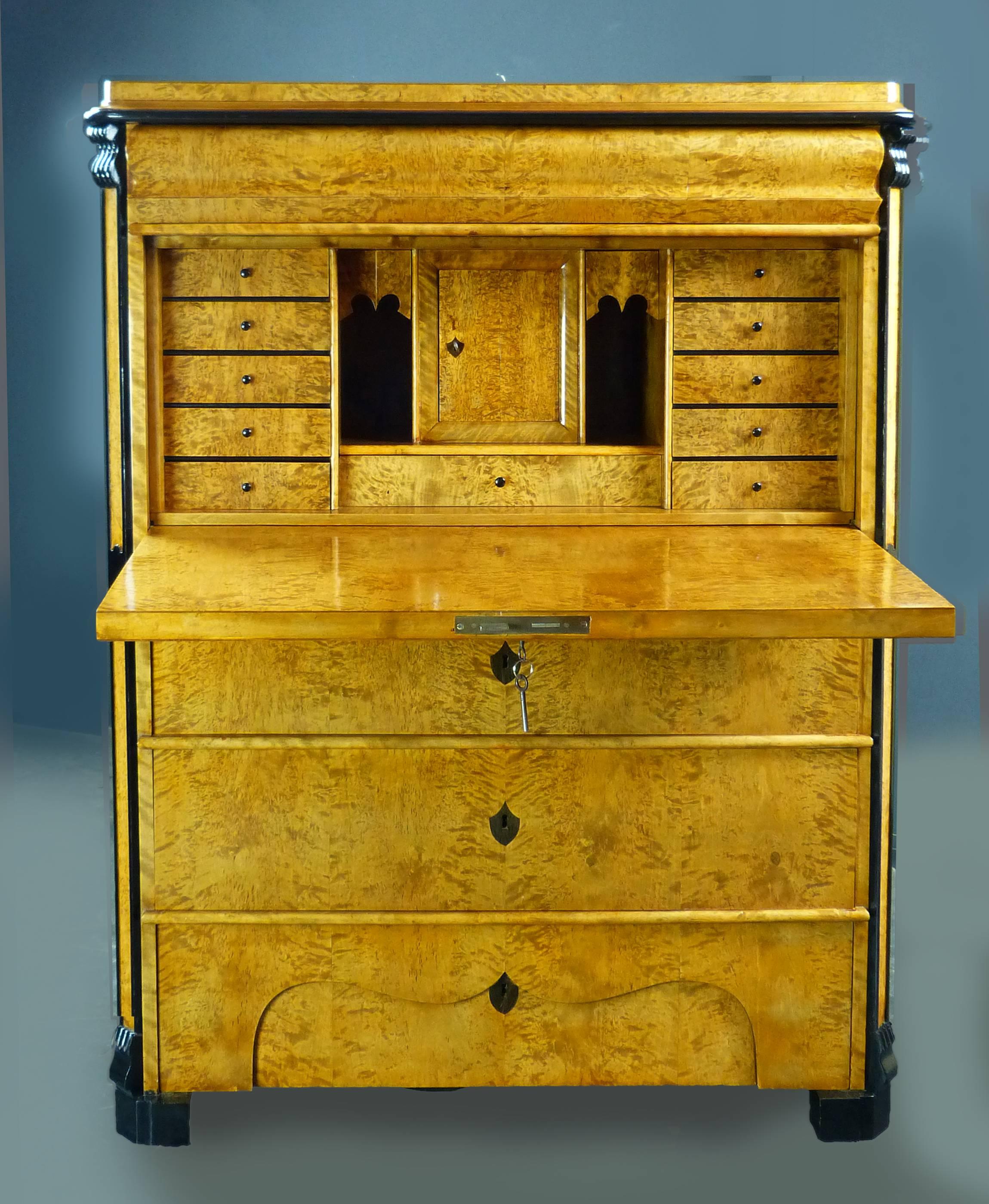 Biedermeier secretaire of small dimensions and of Swedish origin, dating to the beginning of the 19th century, of tiger maple veneer with ebonised frontal corner decorations and carved tops and bottoms. The drawer above the fall-front with moulded