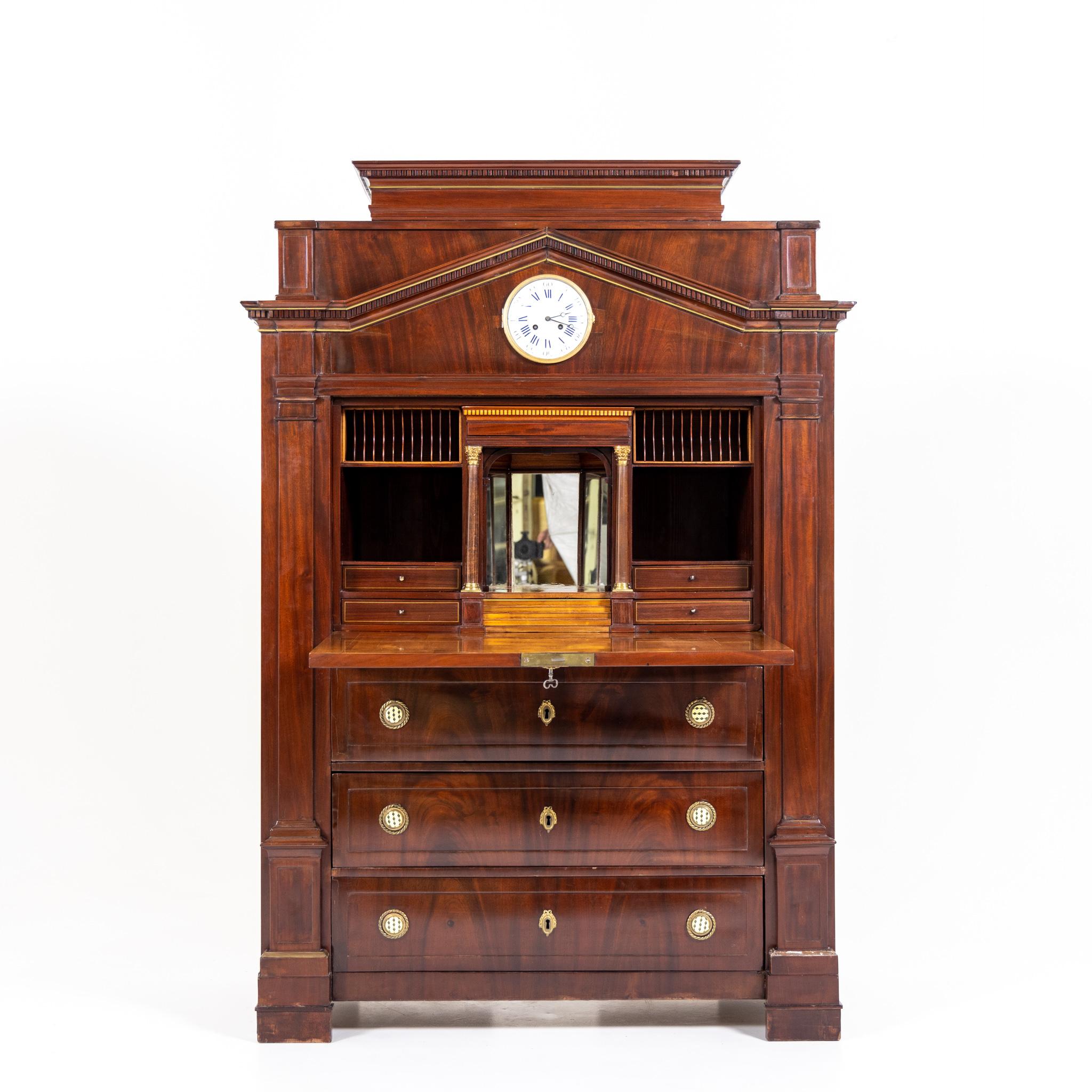 Secretaire with three drawers veneered in mahogany with enameled clock face in the tympanum field of the pedimented top with dentil frieze and brass moldings. Interior division consists of several letter compartments and drawers around a central