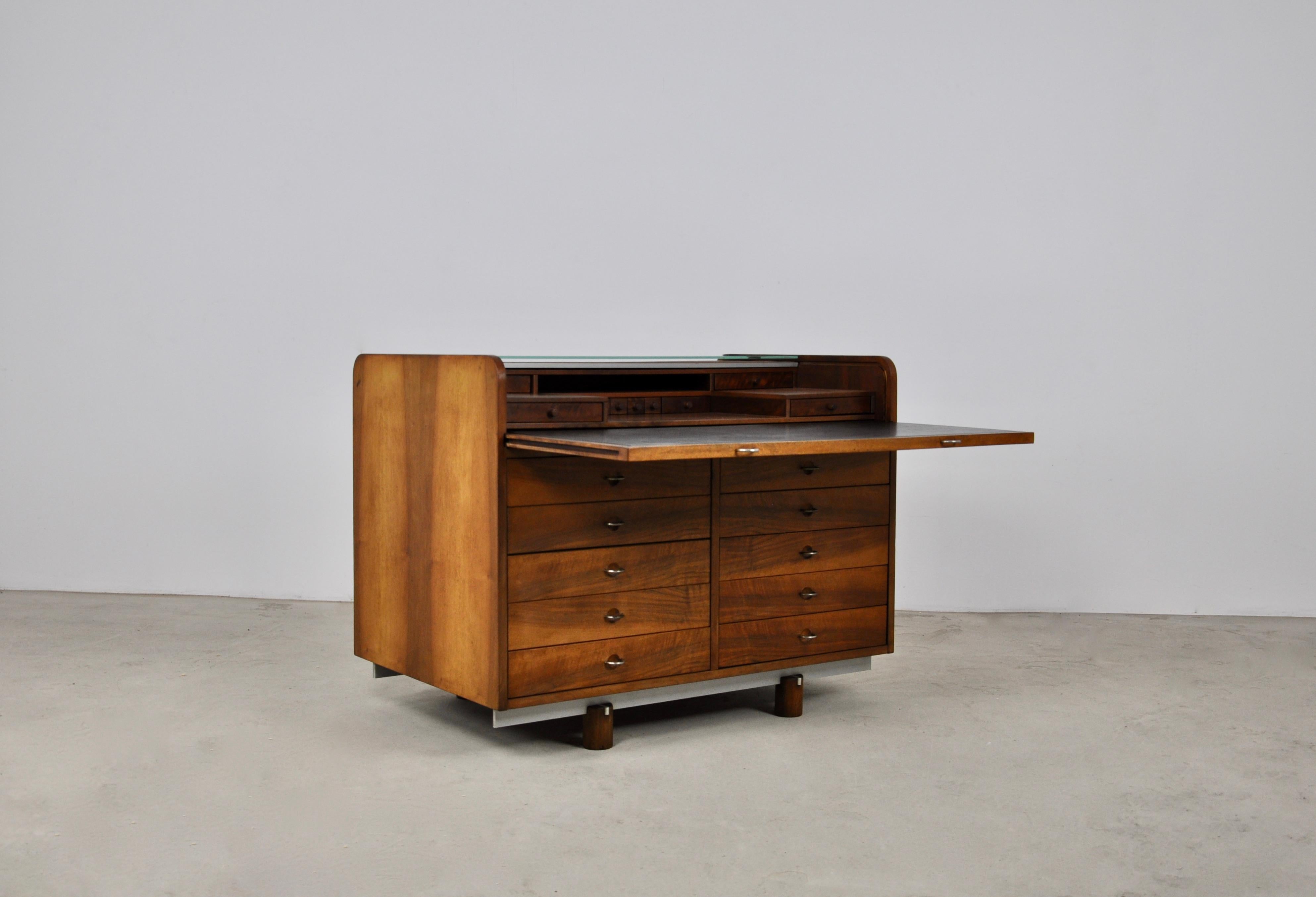 Wooden secretary. The roll top opens by pulling on the leather inlaid writing surface, underneath it are small drawers. This secretary has 10 drawers in the front, several drawers behind the roll top and in the back there are two glass shelves. The