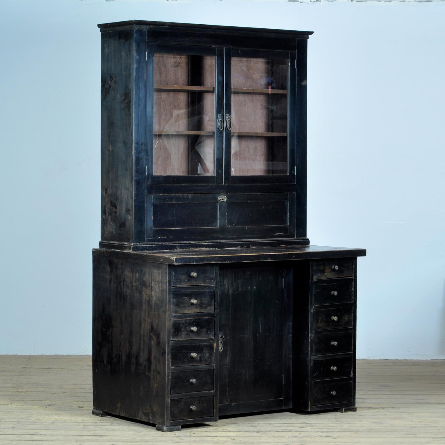 This cabinet dates from circa 1920, produced in Germany. With 12 drawers and a door with a shelf behind it in the lower part. In the upper part a display case and a flap. The cabinet consists of two separate parts.