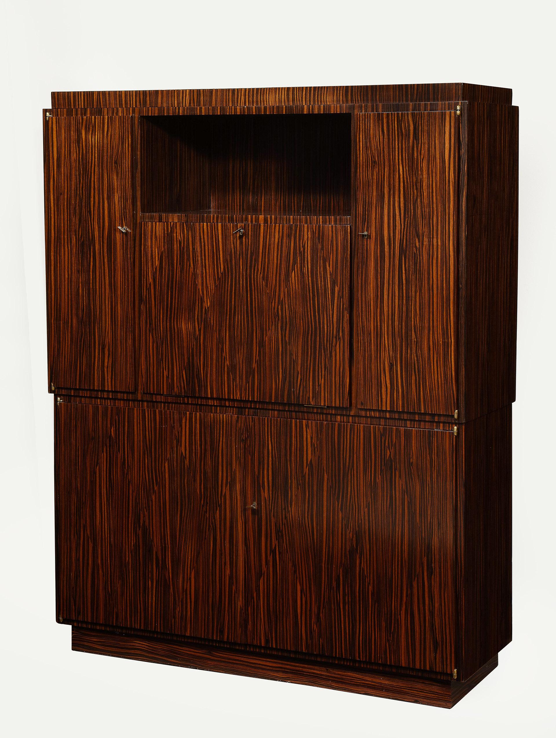 A Macassar ebony secretaire side cabinet with a rectangular stepped top above an open recess and a fall front enclosing a fitted interior, flanked by cupboard doors enclosing shelves above two cupboard doors enclosing shelves on a plinth