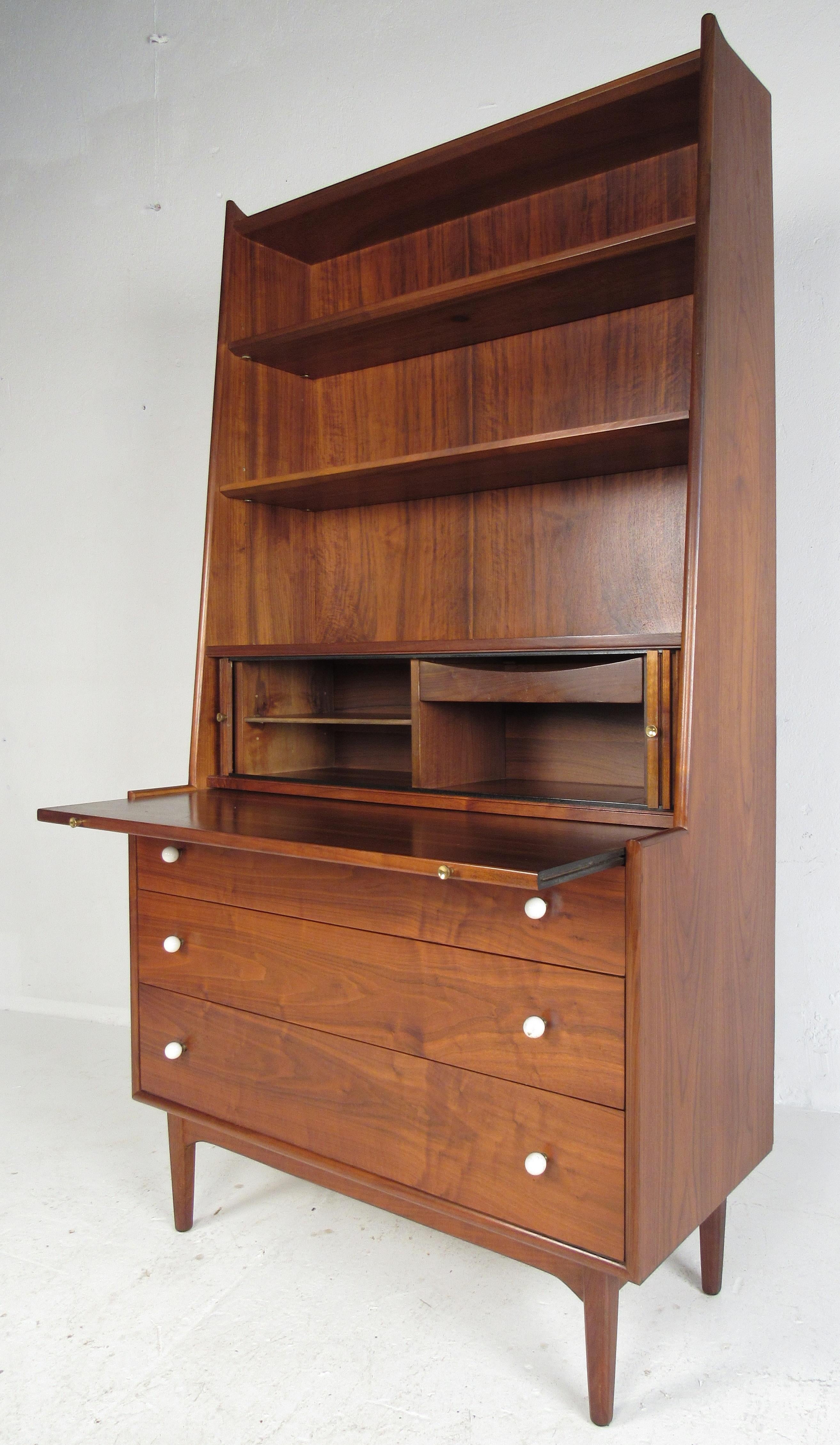 Attractive secretary designed by Kip Stewart featuring two adjustable shelves on top, tambour door storage compartment, three storage drawers below and a pull-out writing surface. The deep rich walnut wood grain contrasts nicely with the white