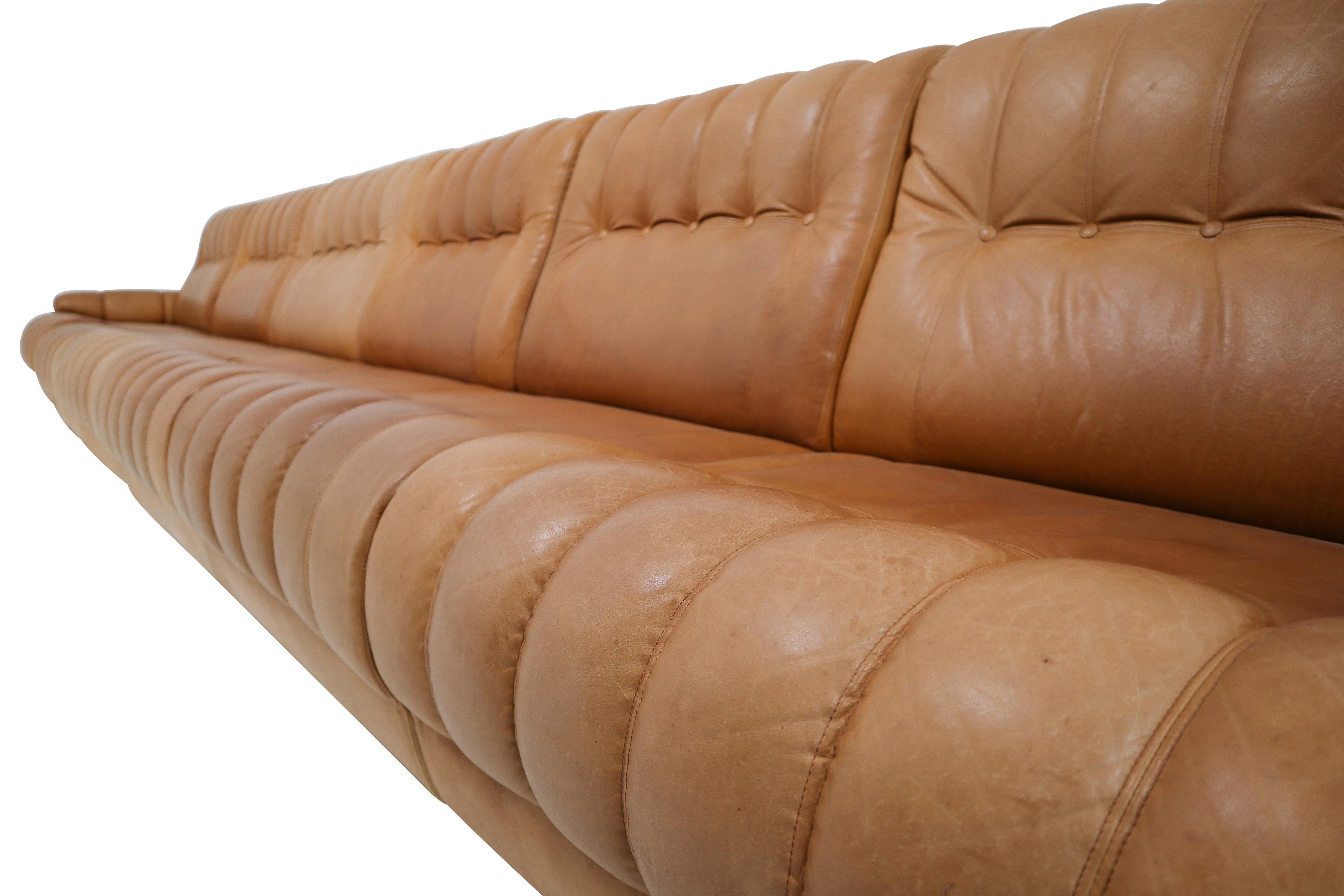 Impressive, 1970s sectional sofa and matching ottoman in cognac leather. Exceptional condition (used distressed patina) and extremely comfortable. This sofa connects in six separate pieces for easy attachment. Stitched leather detailing throughout