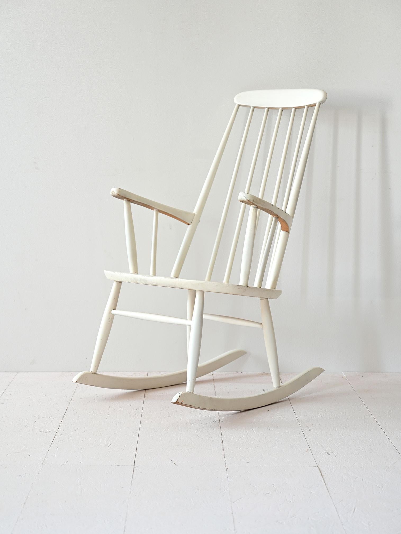 Skandinavischer Schaukelstuhl im Vintage-Stil, weiß lackiert. Er zeichnet sich durch eine markante Rückenlehne mit Holzstäben und ein einfaches, funktionelles Design aus. Er ist ideal für helle und gemütliche Umgebungen und verbindet Tradition und